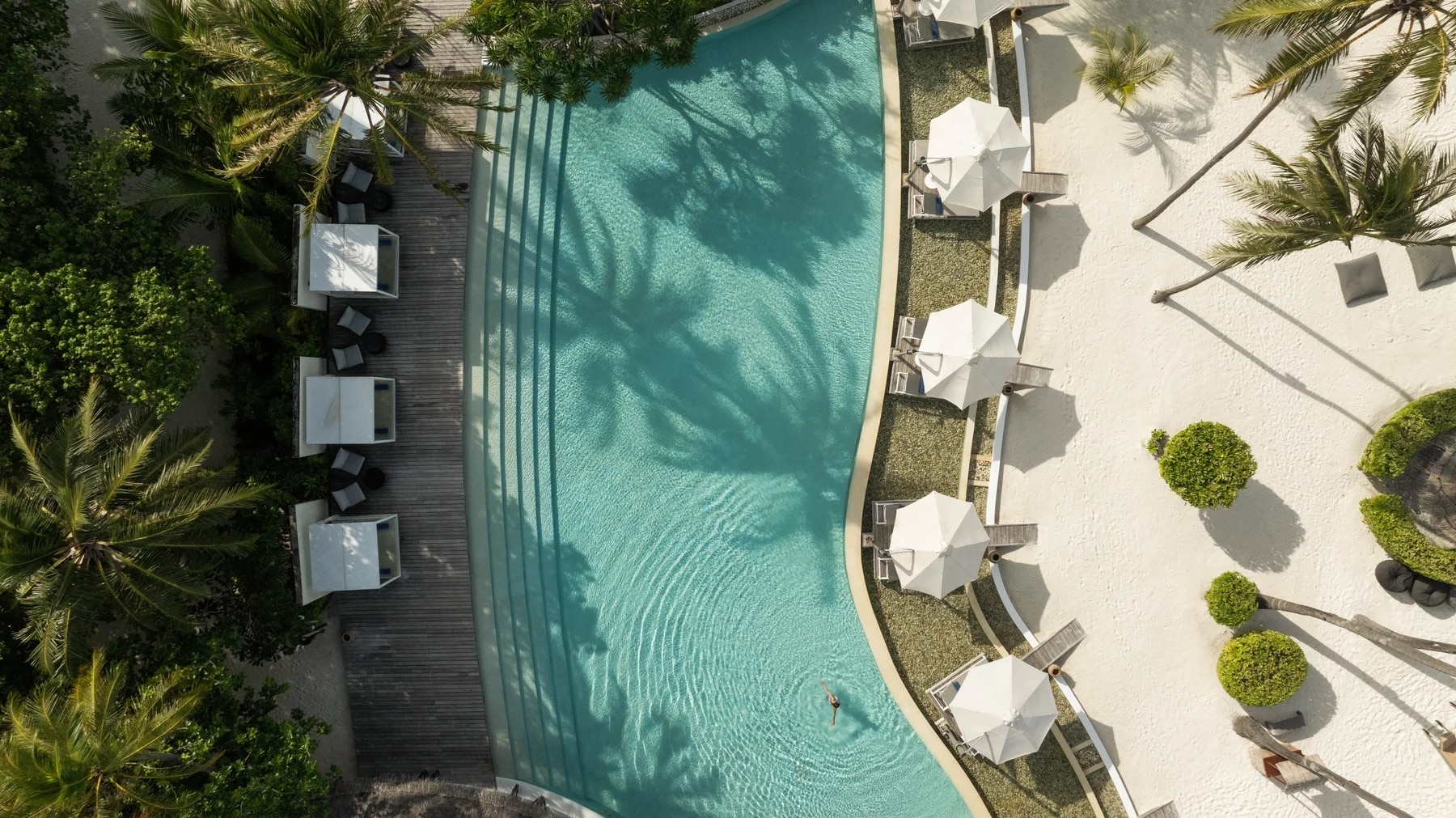 http://Vue%20aérienne%20d'une%20piscine%20de%20resort%20de%20luxe%20entourée%20de%20parasols%20blancs%20et%20de%20végétation%20tropicale.
