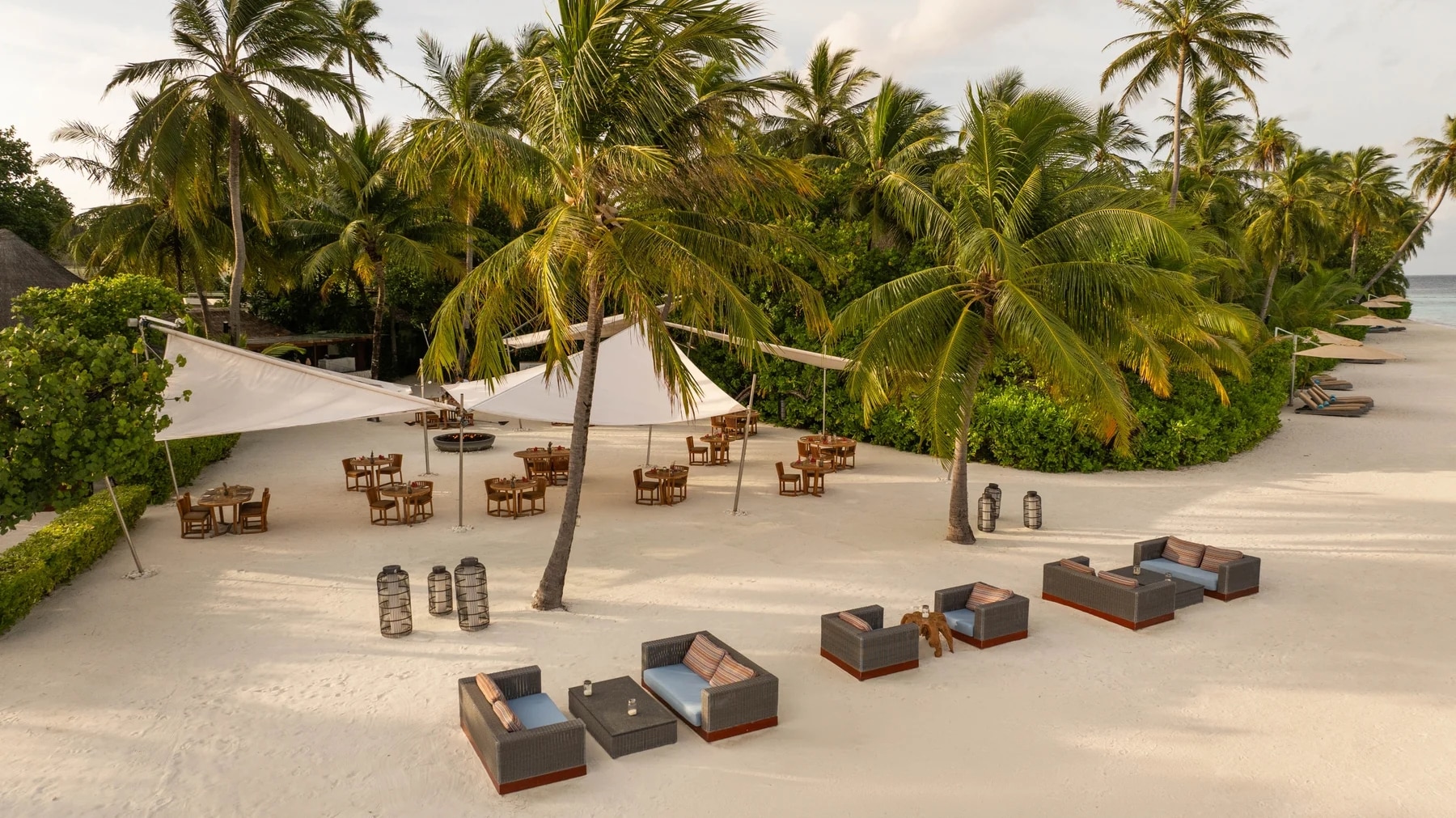 http://Restaurant%20en%20plein%20air%20installé%20sur%20une%20plage%20de%20sable%20blanc%20bordée%20de%20palmiers%20tropicaux.