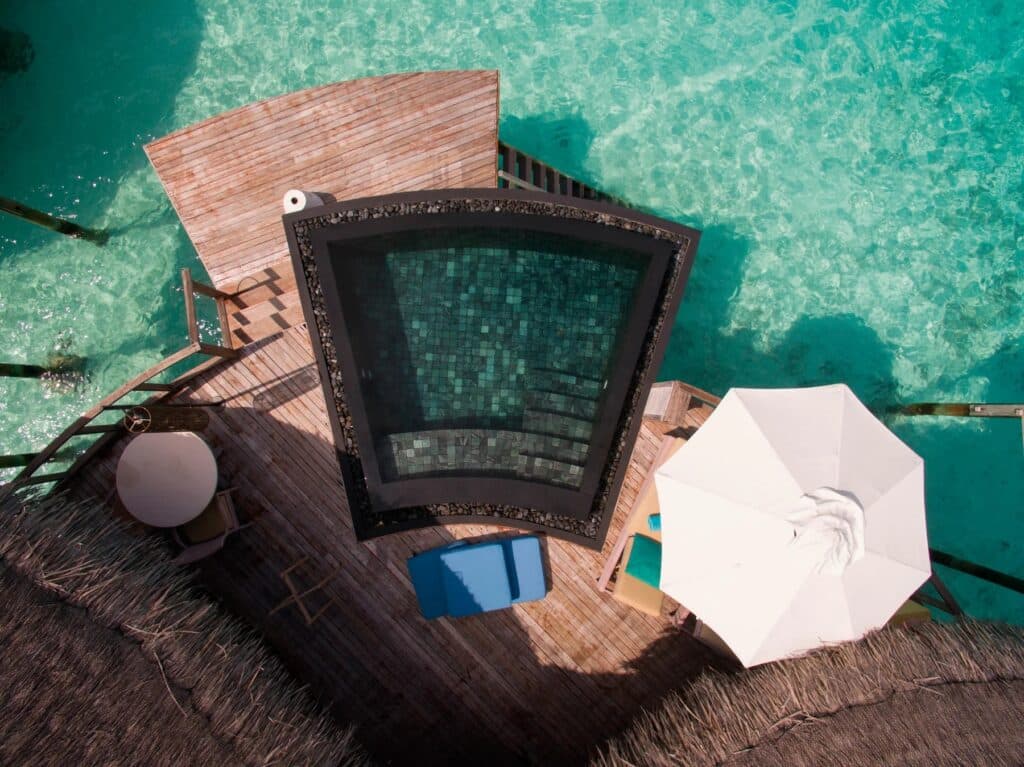 Vue aérienne d'une villa sur pilotis avec piscine privée donnant sur le lagon turquoise des Maldives.