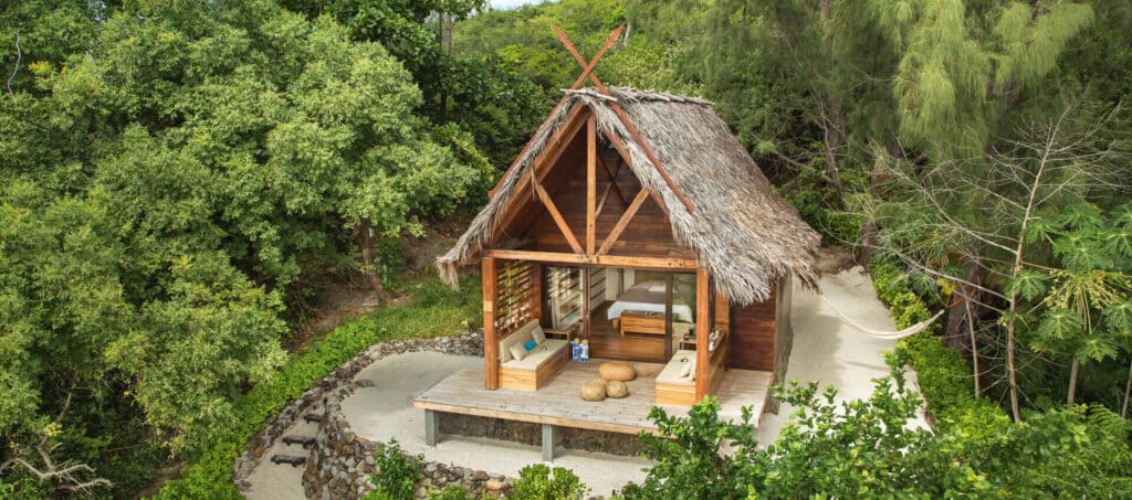 Bungalow avec toit en feuilles de palmier, entouré de végétation tropicale