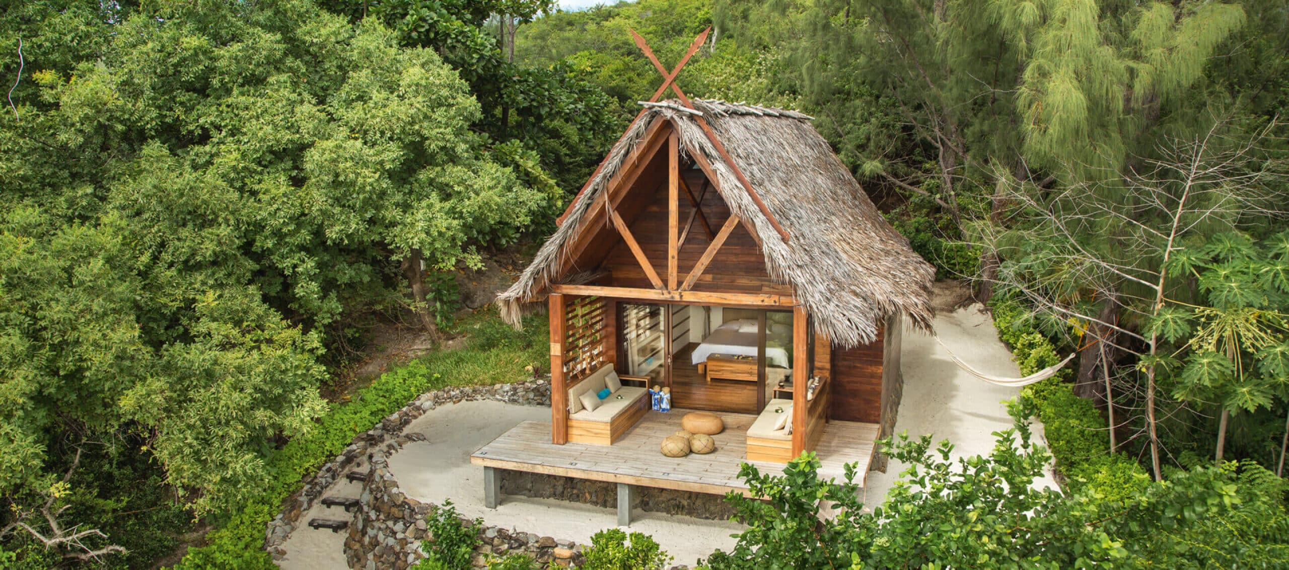 http://Bungalow%20avec%20toit%20en%20feuilles%20de%20palmier,%20entouré%20de%20végétation%20tropicale