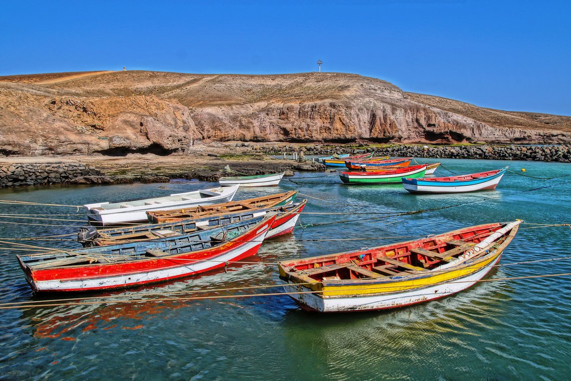 http://Barques%20de%20pêche%20multicolores%20amarrées%20dans%20une%20crique%20bordée%20de%20collines%20arides.