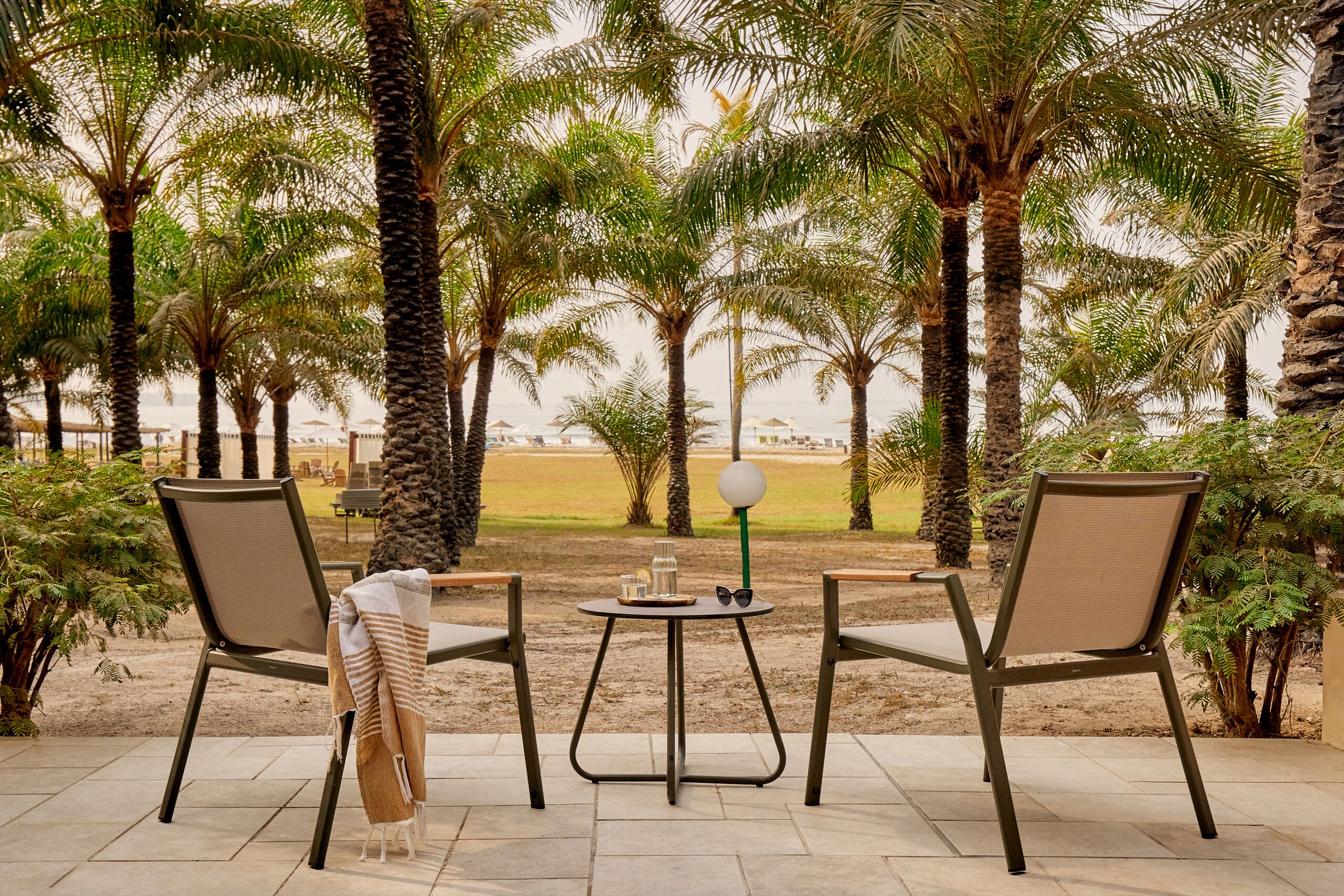 http://Deux%20fauteuils%20et%20une%20table%20sur%20une%20terrasse%20ombragée%20entourée%20de%20palmiers,%20avec%20vue%20sur%20la%20plage