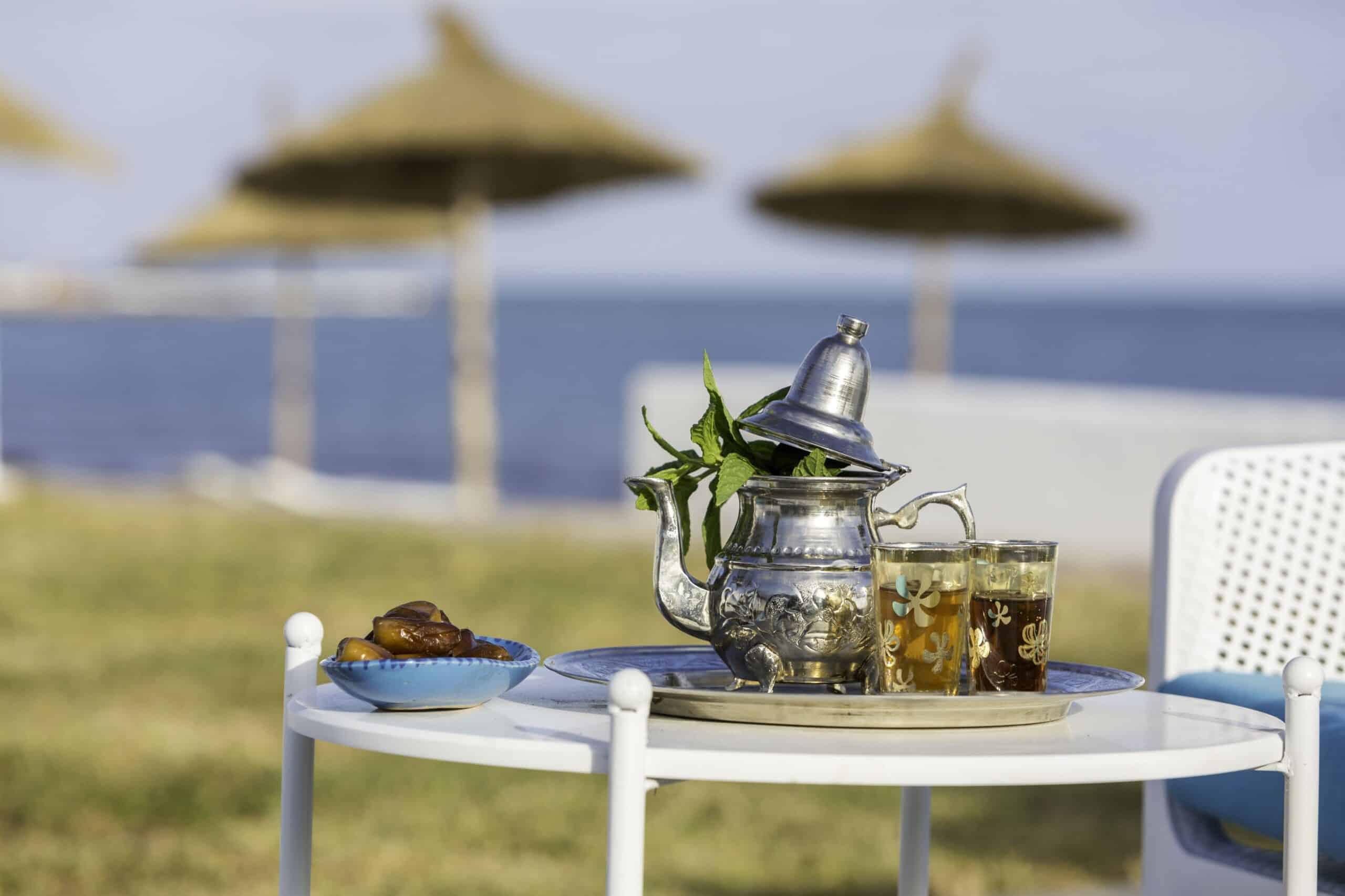 http://Plateau%20en%20argent%20avec%20théière%20marocaine,%20verres%20à%20thé%20et%20dattes%20sur%20une%20table%20près%20de%20la%20mer