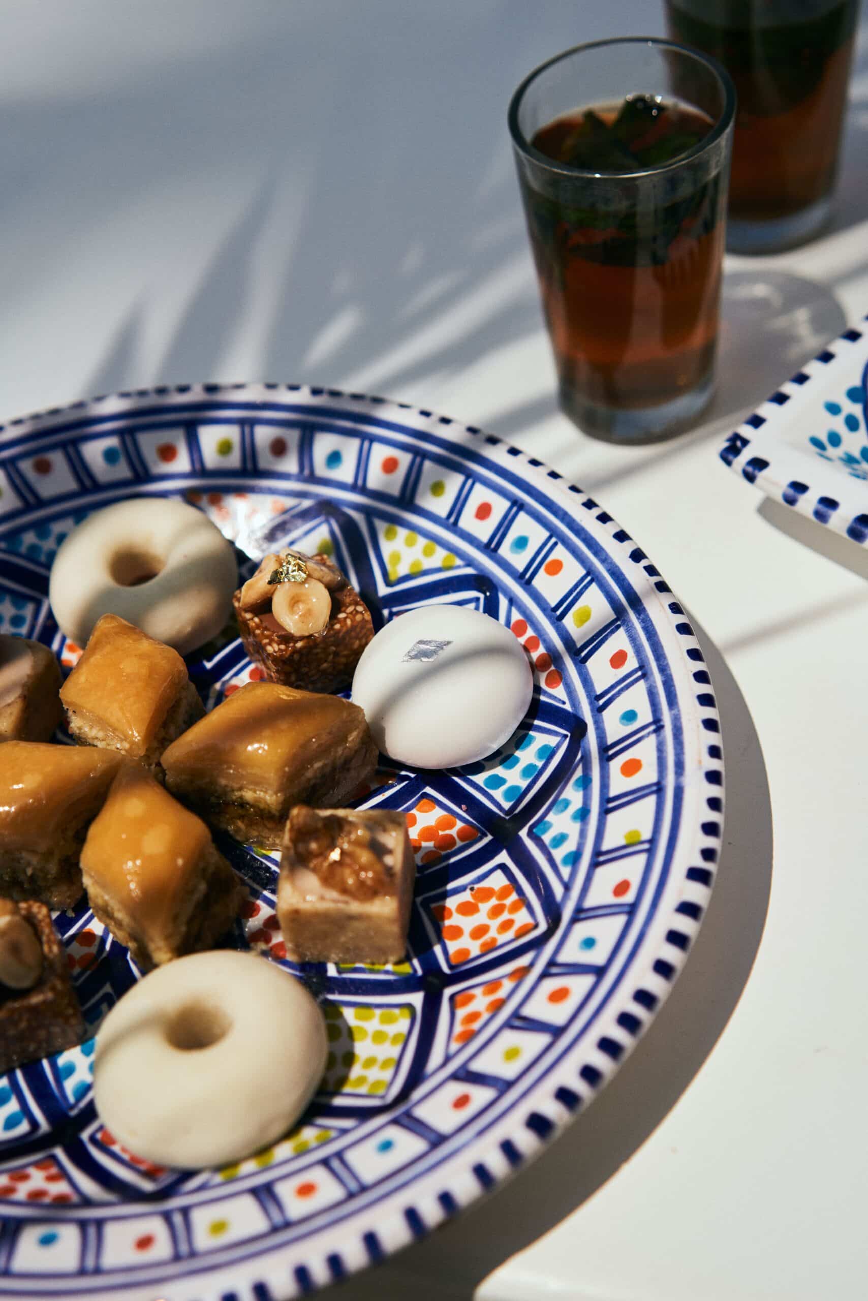 http://Plateau%20coloré%20de%20pâtisseries%20orientales%20avec%20verres%20de%20thé%20à%20la%20menthe%20sur%20une%20table%20blanche