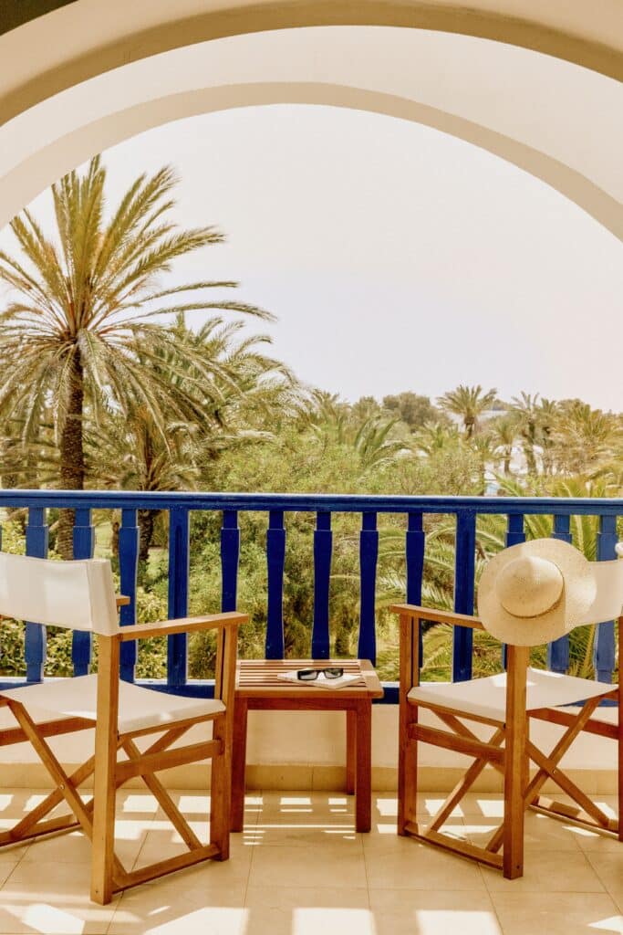 Deux fauteuils et une table sur un balcon avec vue sur une palmeraie luxuriante