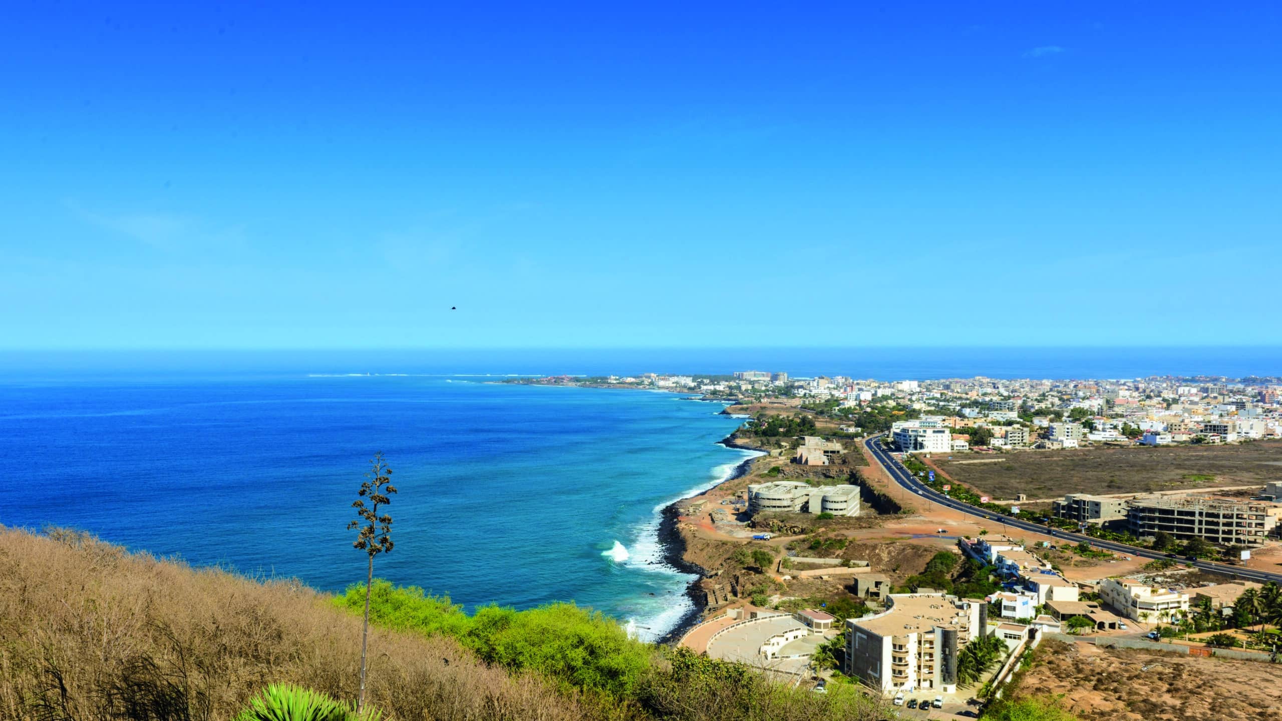 http://Vue%20panoramique%20sur%20la%20côte%20atlantique%20de%20Dakar%20avec%20route%20côtière,%20bâtiments%20modernes%20et%20mer%20bleue.