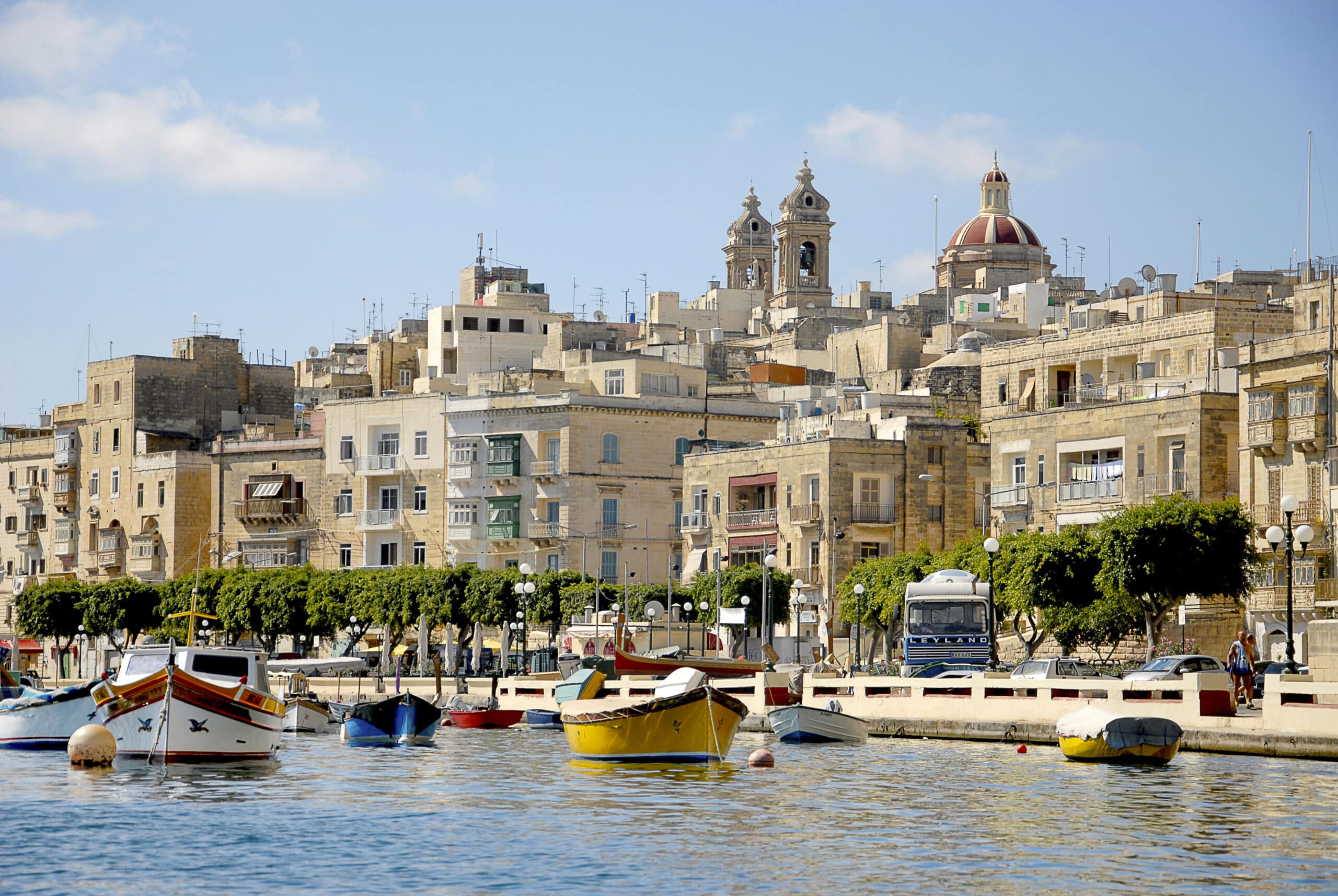http://Vue%20sur%20des%20bateaux%20colorés%20amarrés%20dans%20un%20port%20maltais%20bordé%20d’immeubles%20anciens%20et%20d’une%20église%20baroque.