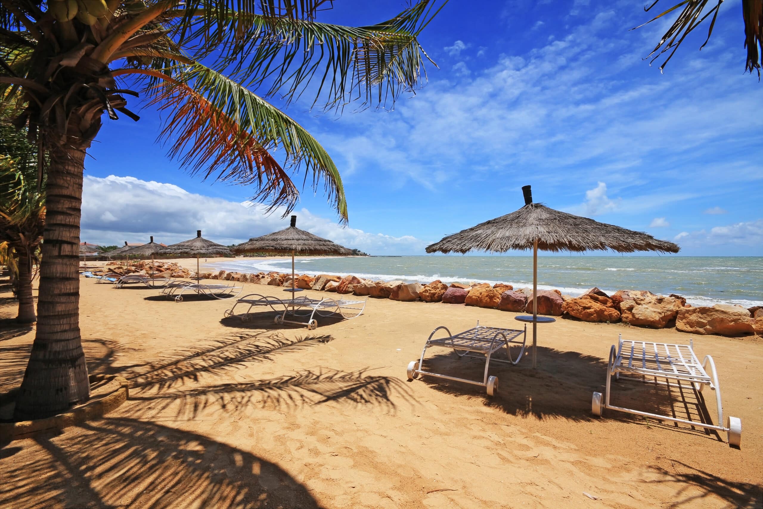 http://Chaises%20longues%20et%20parasols%20en%20paillote%20sur%20une%20plage%20de%20sable%20doré%20à%20Saly,%20au%20Sénégal.