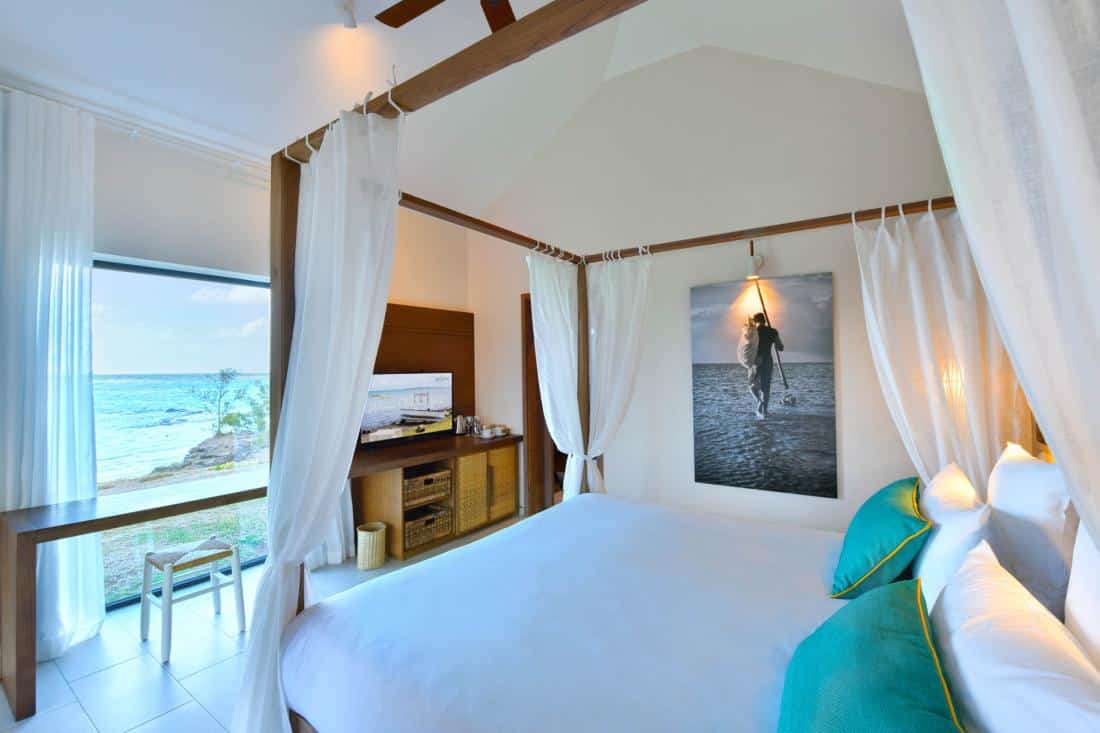 http://Intérieur%20d’une%20chambre%20de%20bungalow%20avec%20lit%20double,%20coin%20salon,%20et%20grande%20baie%20vitrée%20donnant%20sur%20la%20mer.