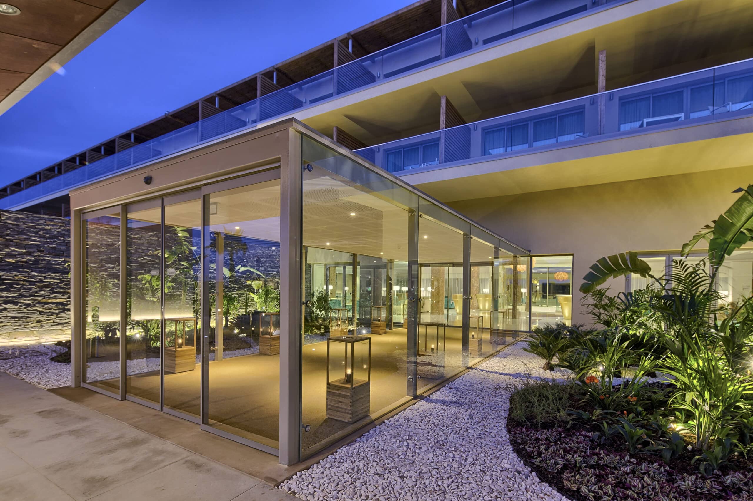 http://Entrée%20vitrée%20d’un%20hôtel%20design%20éclairée%20en%20soirée.