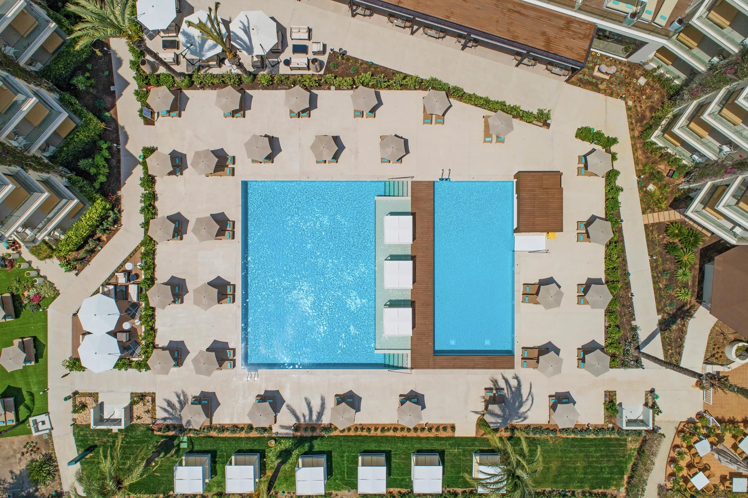 http://Vue%20aérienne%20d'une%20grande%20piscine%20design%20entourée%20de%20transats%20et%20de%20parasols%20dans%20un%20complexe%20hôtelier.