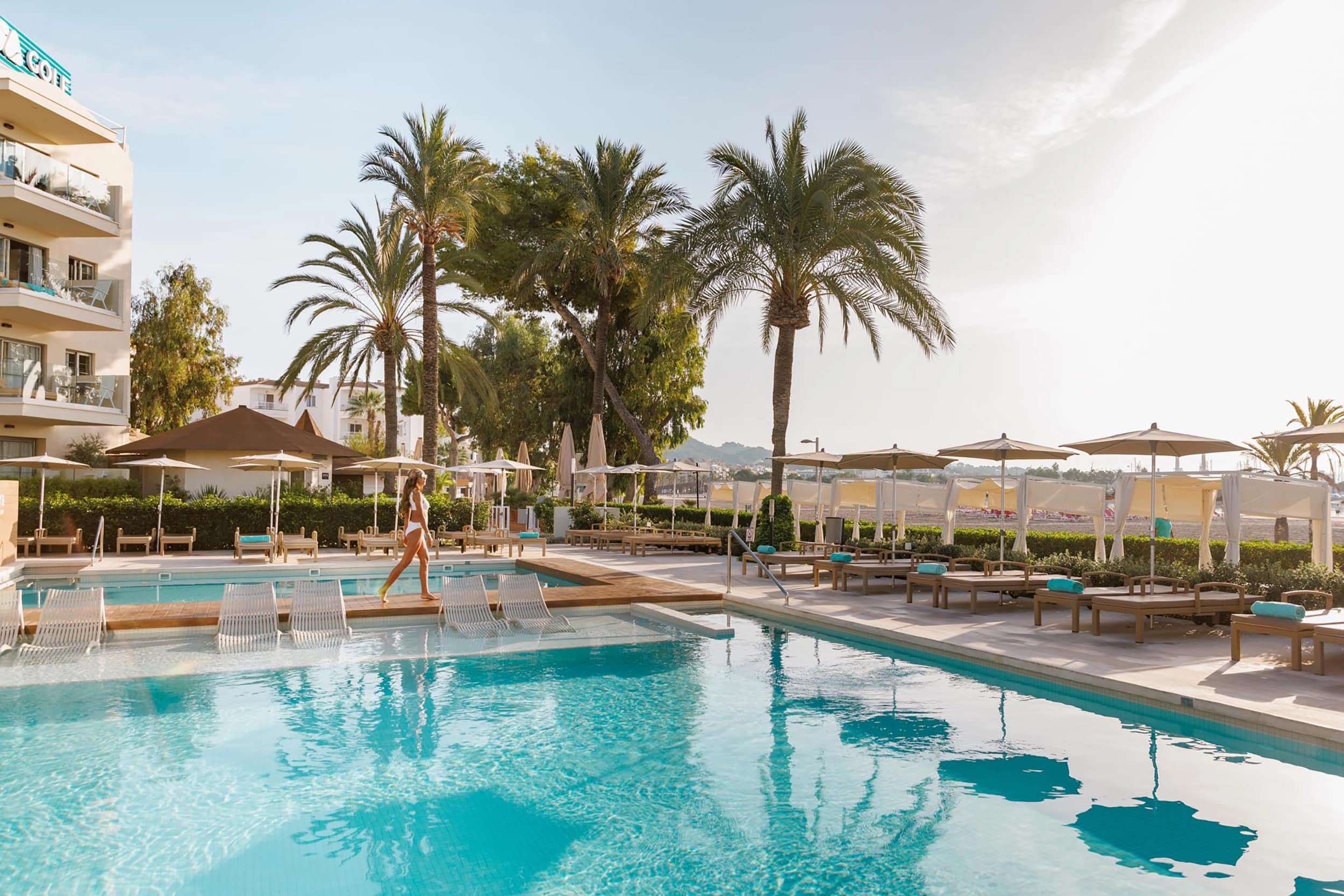 http://Piscine%20extérieure%20avec%20palmiers,%20transats%20et%20parasols%20dans%20un%20hôtel%20sous%20le%20soleil.