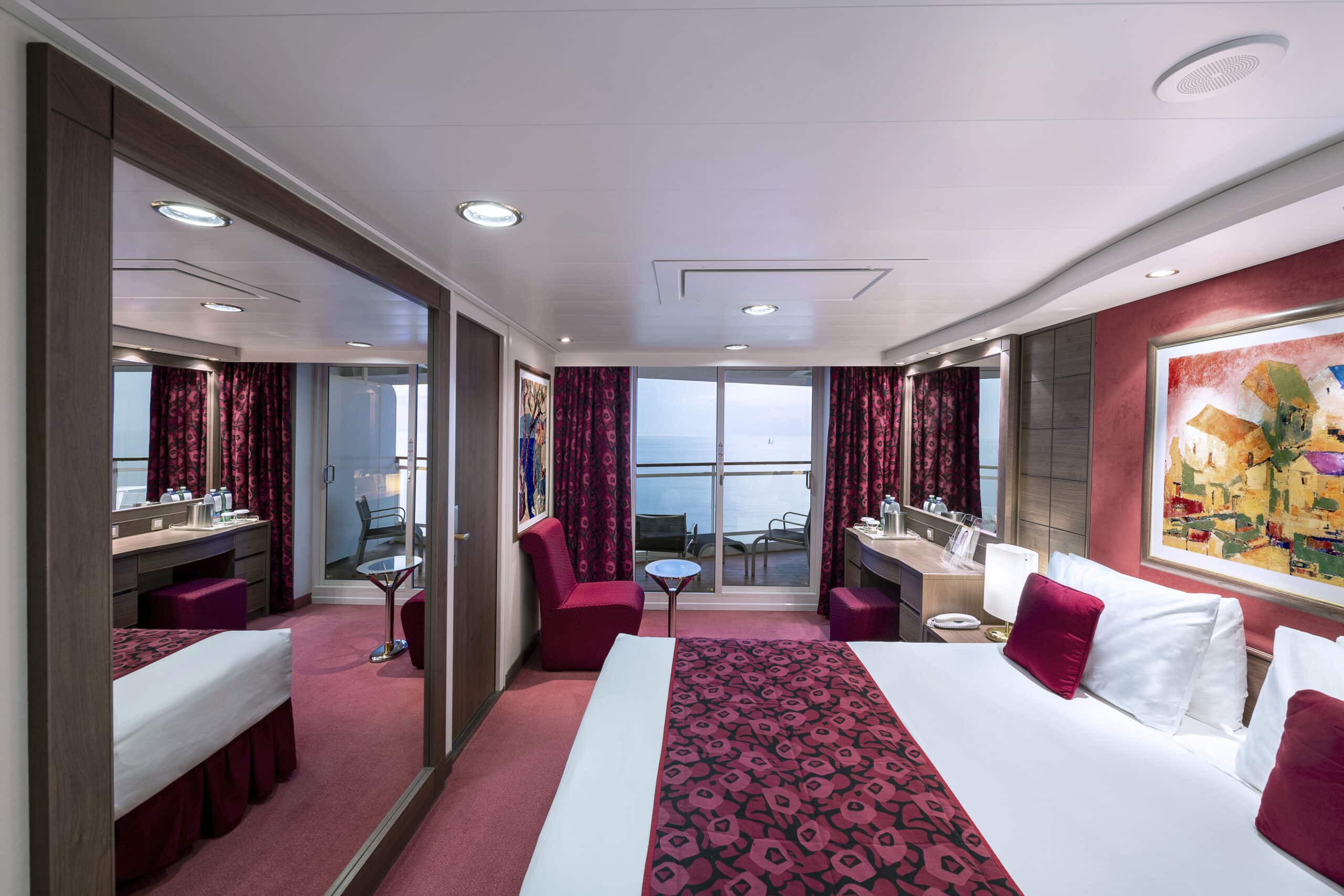Cabine avec balcon du MSC Orchestra comprenant un lit double, une décoration bordeaux et un espace extérieur avec vue sur la mer.