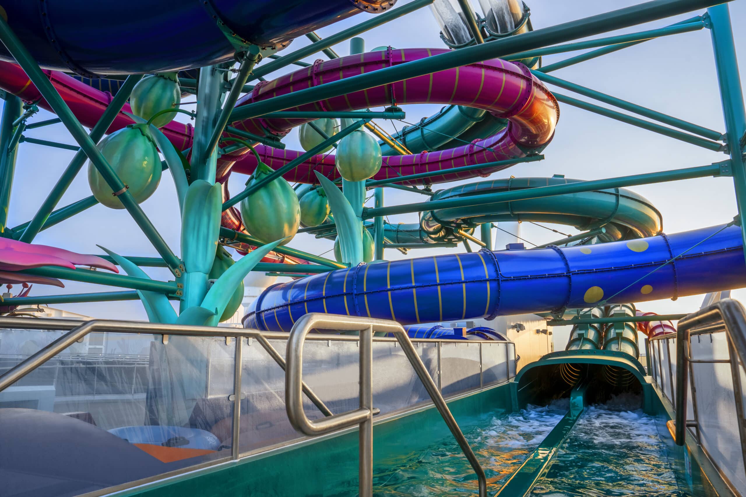MSC World Europa - Toboggans aquatiques multicolores en spirale sur le pont d'un navire de croisière, avec bassin de réception et structures décoratives tropicales.