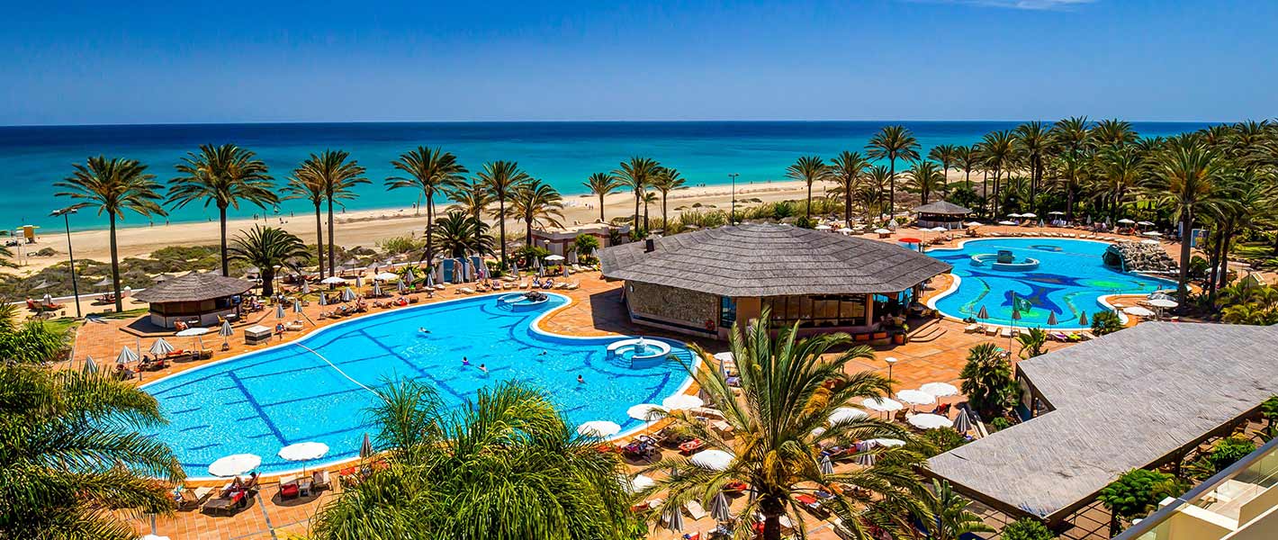 http://Vue%20panoramique%20sur%20un%20hôtel%20en%20bord%20de%20mer%20avec%20piscines,%20palmiers%20et%20plage%20de%20sable%20fin.