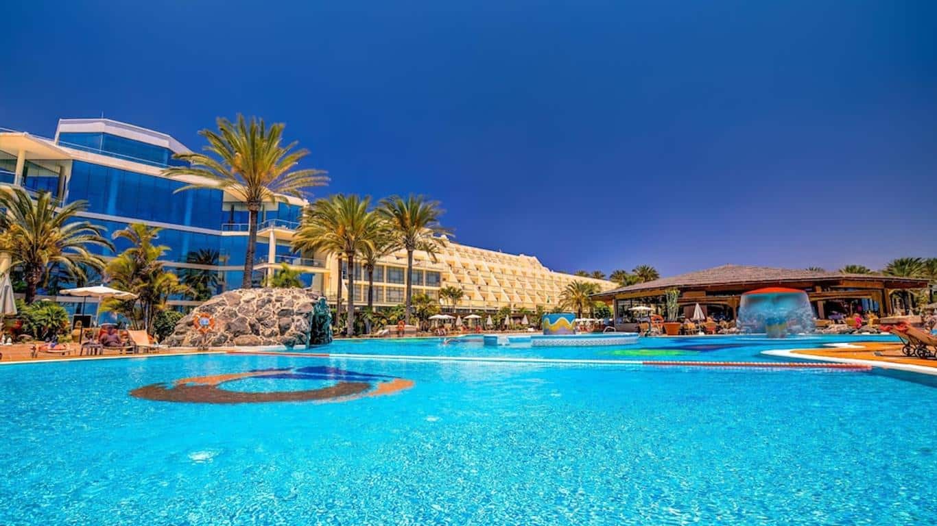 http://Grande%20piscine%20extérieure%20entourée%20de%20palmiers%20avec%20bar%20central%20dans%20un%20hôtel%20en%20bord%20de%20mer.