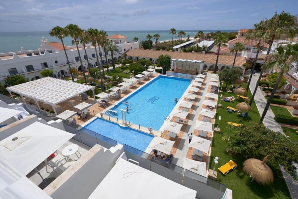 Vue en hauteur de la piscine extérieure de l’hôtel La Playa avec ses jardins et la mer en arrière-plan.