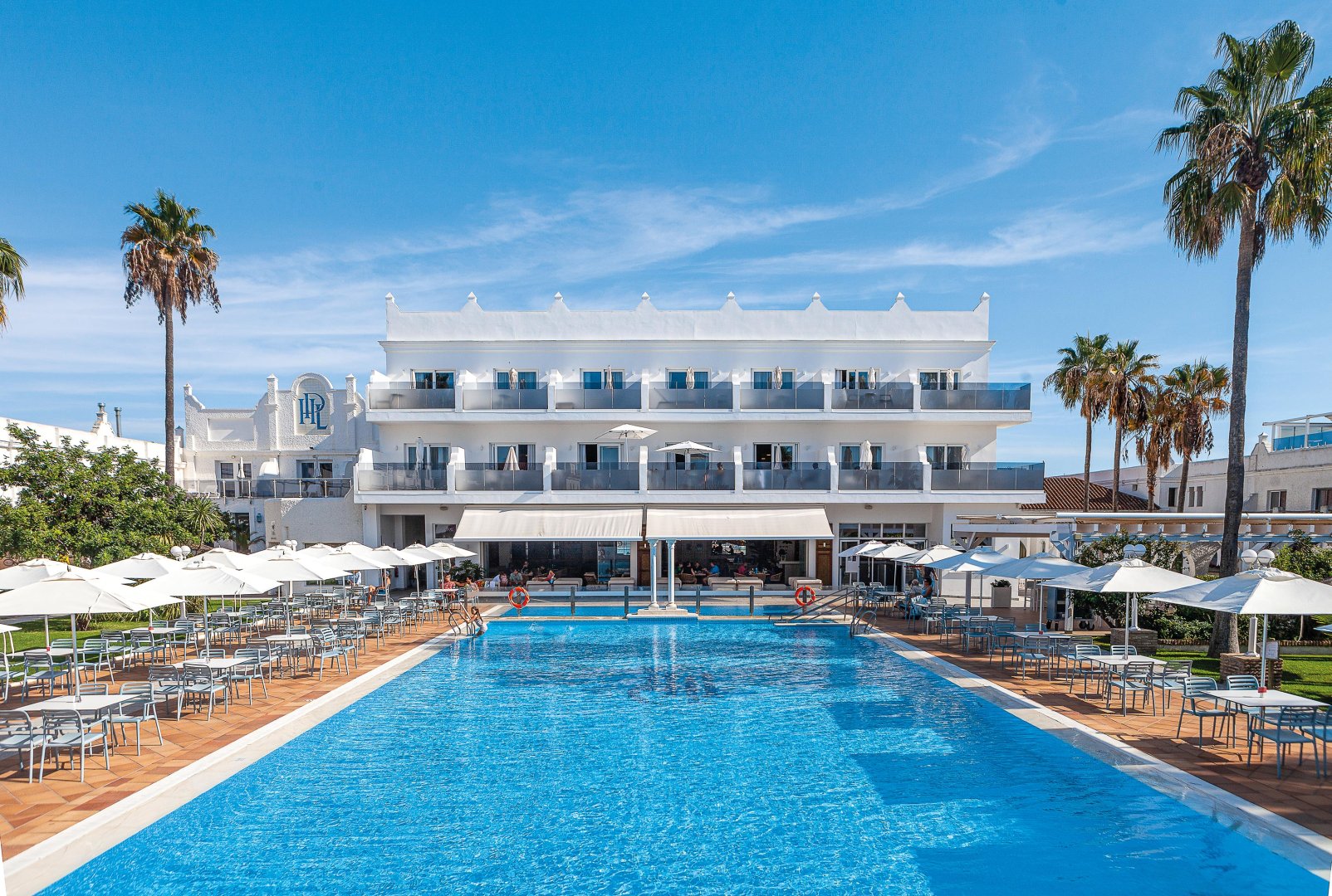 http://Grande%20piscine%20extérieure%20bordée%20de%20transats%20devant%20la%20façade%20blanche%20de%20l’hôtel%20La%20Playa.