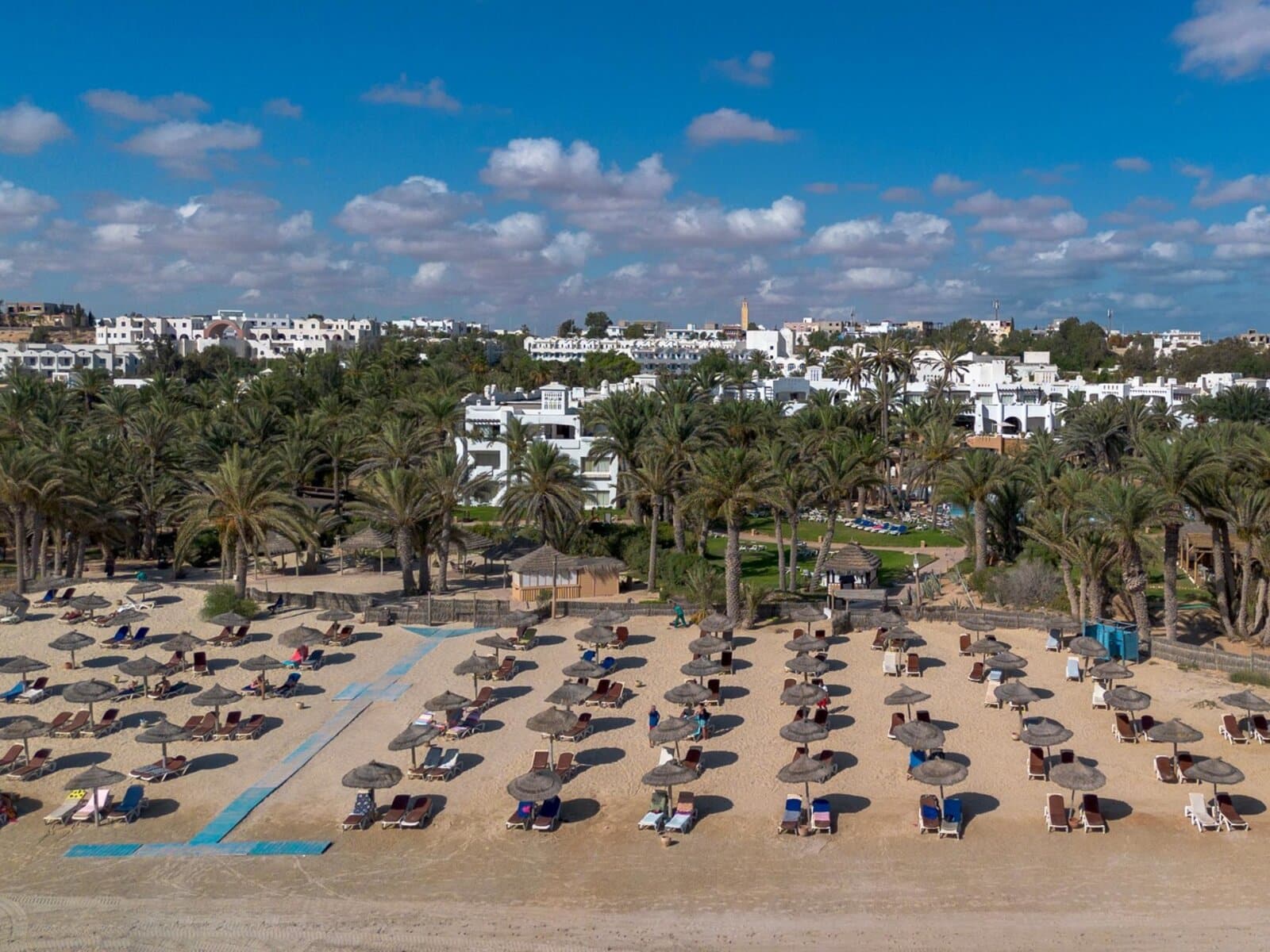 http://Plage%20de%20sable%20fin%20équipée%20de%20transats%20et%20parasols%20en%20paille%20devant%20un%20hôtel%20à%20Djerba.