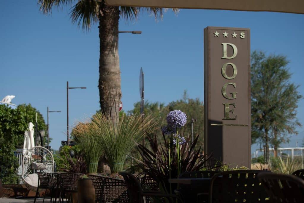 Enseigne de l’hôtel Doge quatre étoiles entourée de végétation et de mobilier extérieur.