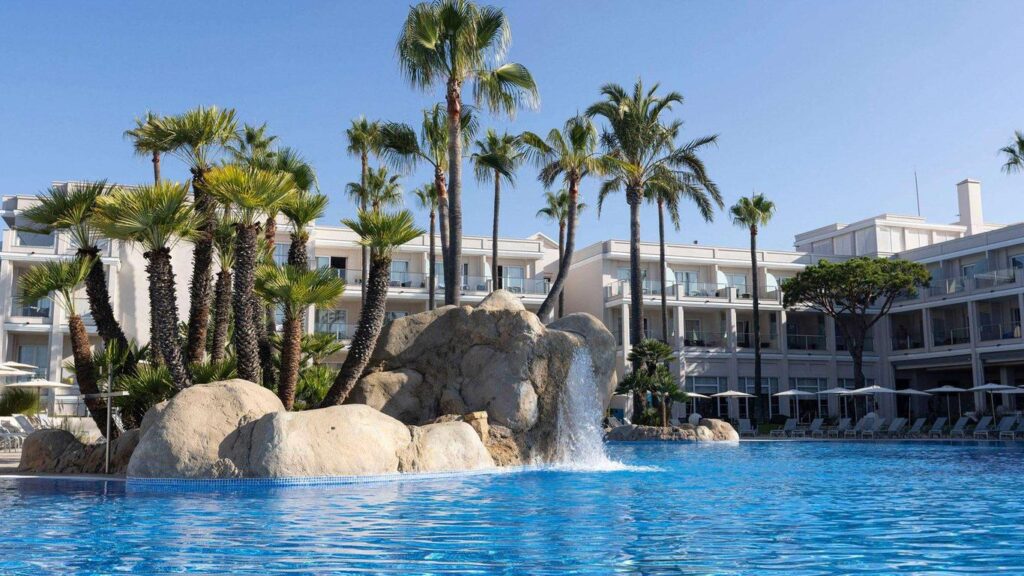 Îlot rocheux avec cascade et palmiers au centre de la piscine d’un hôtel de luxe.