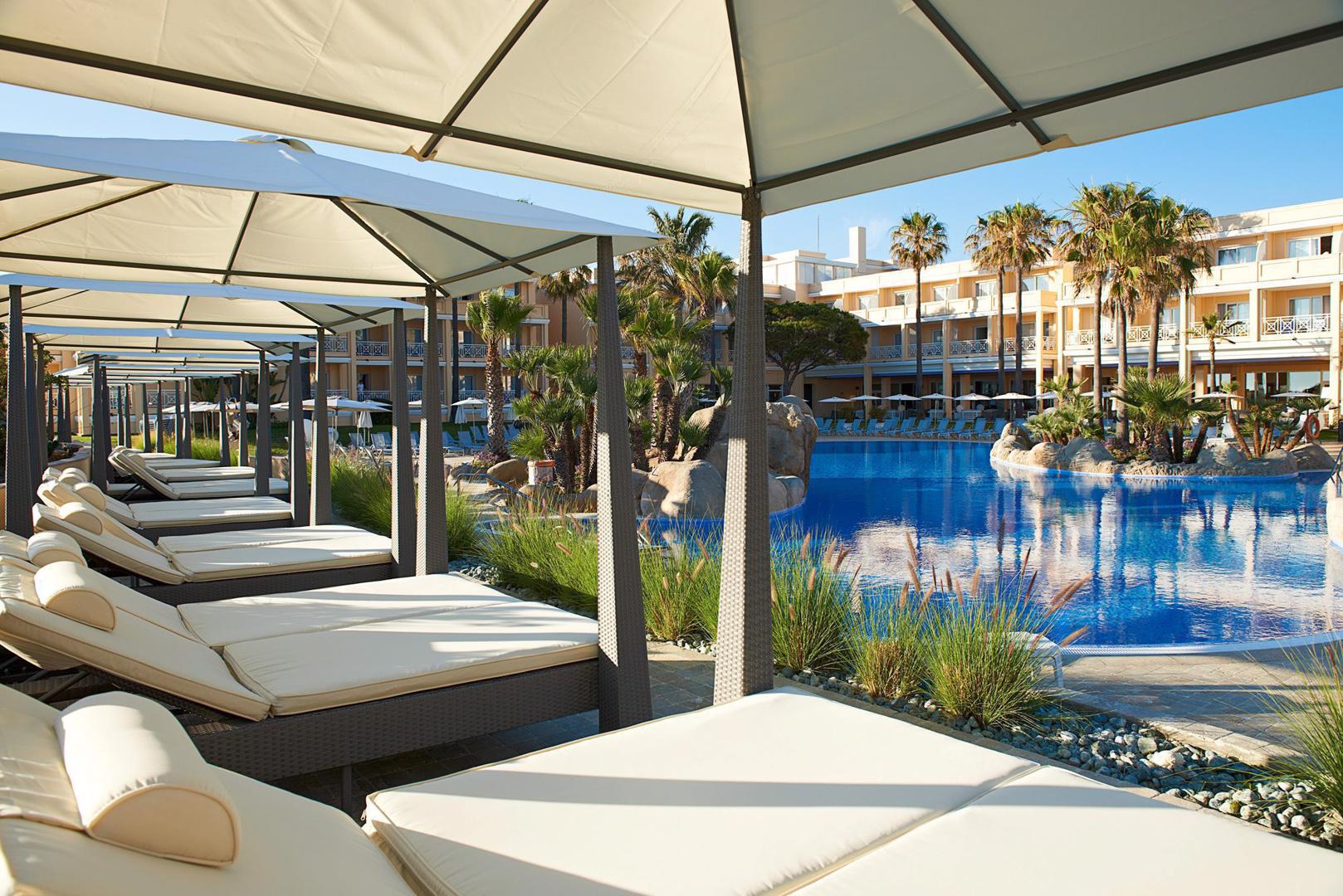 http://Lits%20balinais%20avec%20parasols%20au%20bord%20d’une%20grande%20piscine%20entourée%20de%20palmiers.