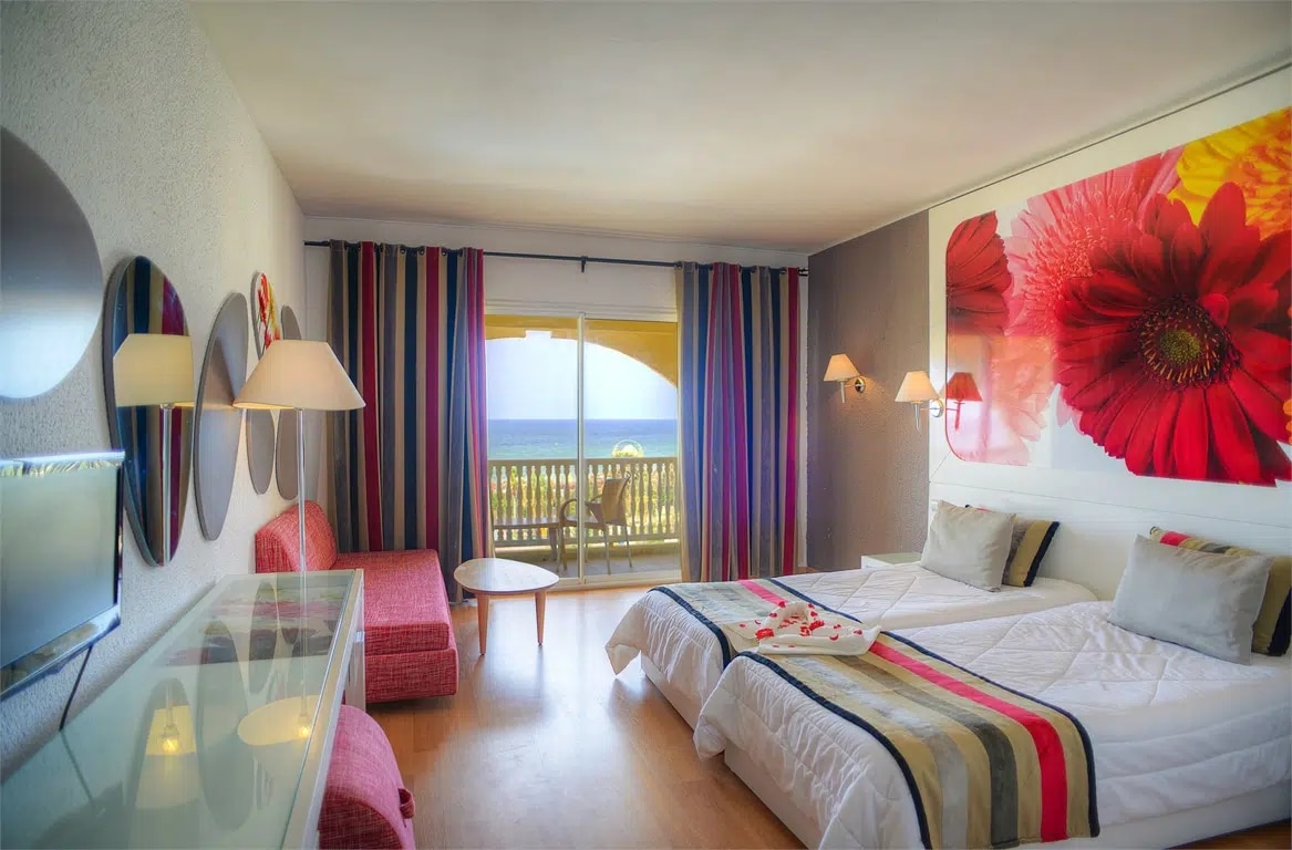 http://Chambre%20d’hôtel%20moderne%20avec%20deux%20lits%20simples,%20décoration%20florale%20et%20balcon%20vue%20mer.