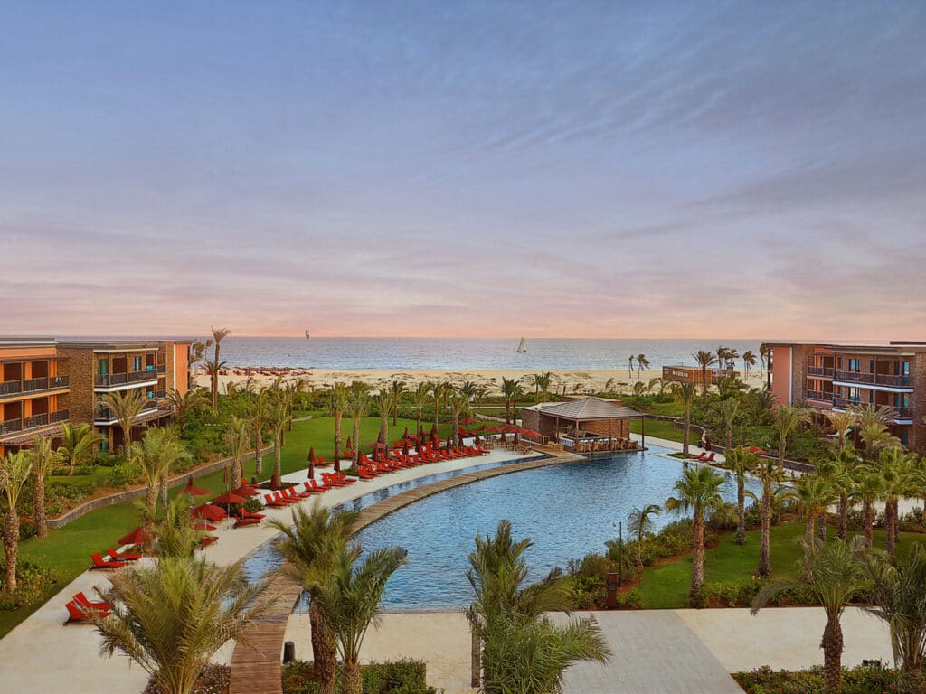 Vue panoramique d’un resort de luxe au Cap-Vert avec piscine lagon, palmiers et accès direct à la plage.