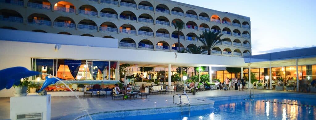 Hôtel en soirée avec piscine illuminée et clients profitant de l’ambiance extérieure.