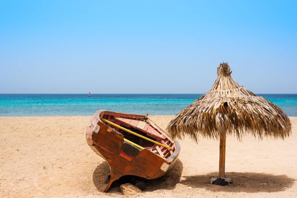 Barque en bois renversée et parasol en paille sur une plage de sable fin au Cap-Vert