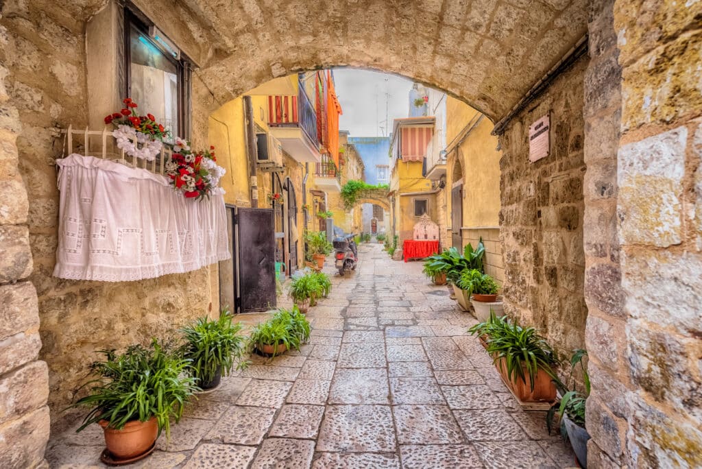 Ruelle pavée colorée et fleurie de Bari Vecchia avec plantes en pots et linge suspendu.