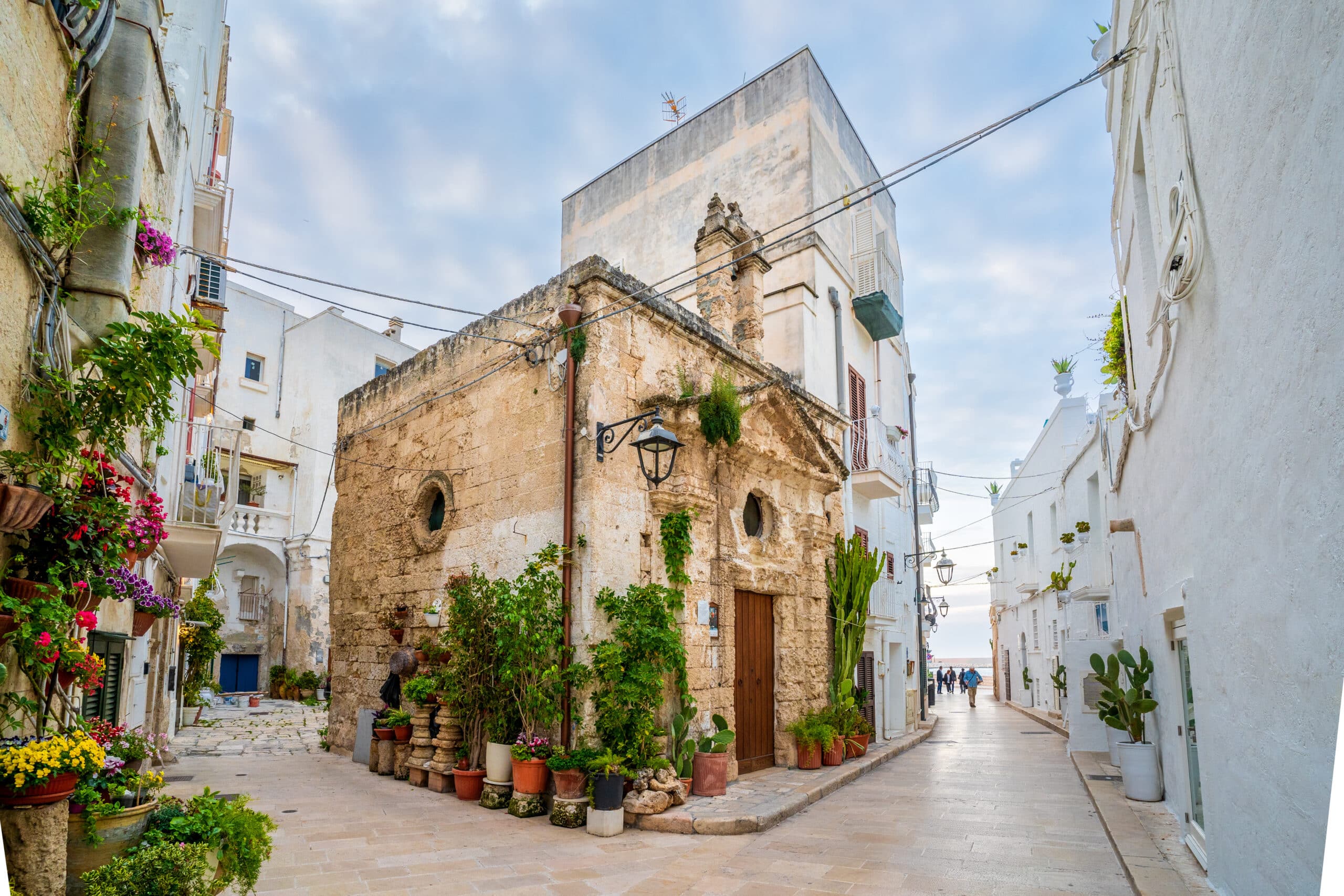 http://Ancienne%20bâtisse%20en%20pierre%20entourée%20de%20pots%20de%20fleurs%20dans%20une%20ruelle%20de%20Polignano%20a%20Mare.