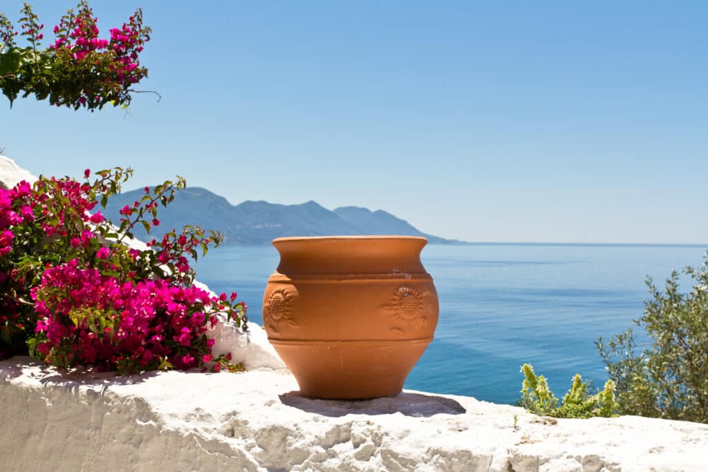 Vase en terre cuite sur un muret blanc avec vue sur la mer Méditerranée et les montagnes grecques