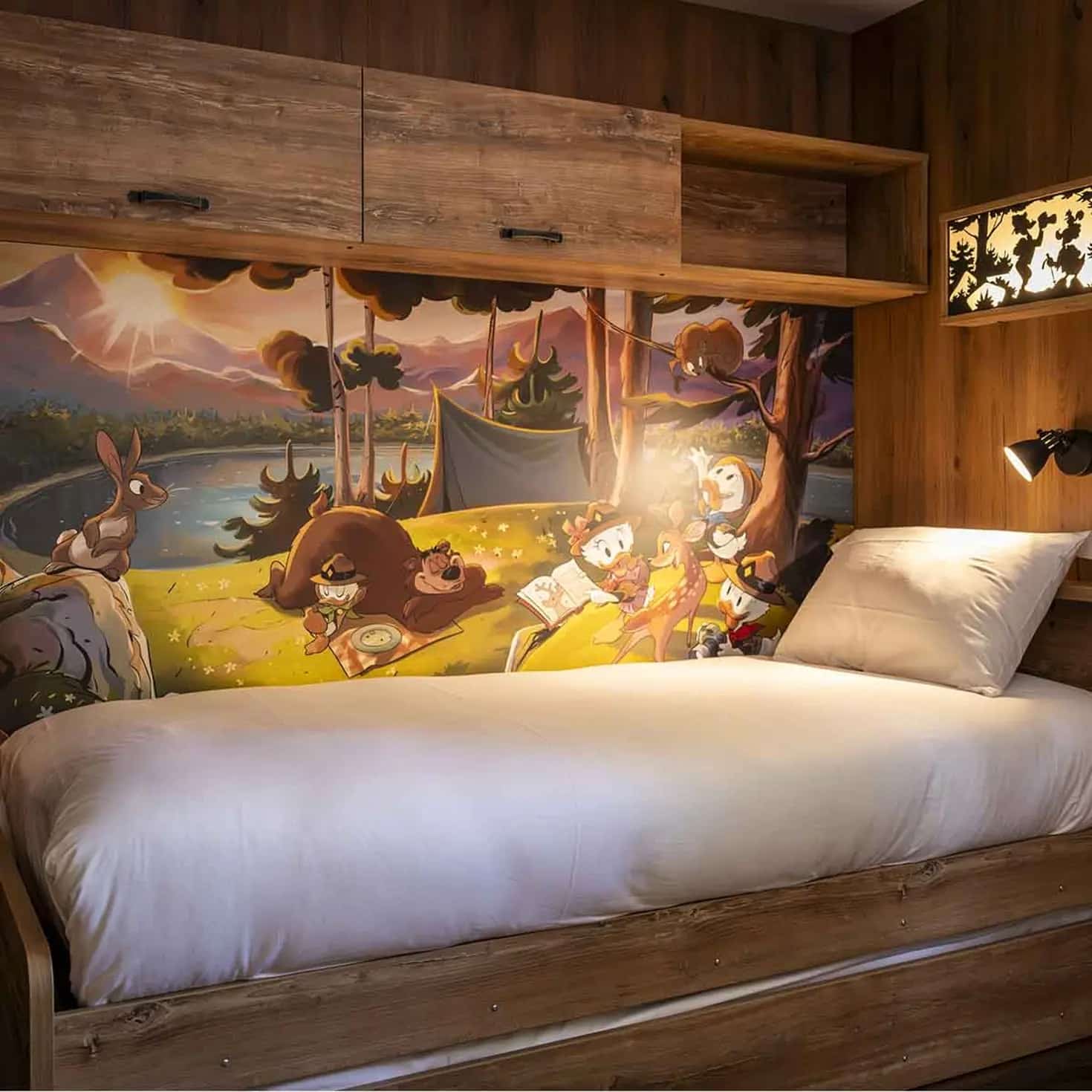 http://Lit%20simple%20dans%20une%20chambre%20d’enfant%20avec%20une%20fresque%20murale%20Disney%20sur%20le%20thème%20de%20la%20forêt.