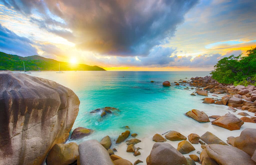 Coucher de soleil sur une plage de sable blanc bordée de rochers granitiques aux Seychelles
