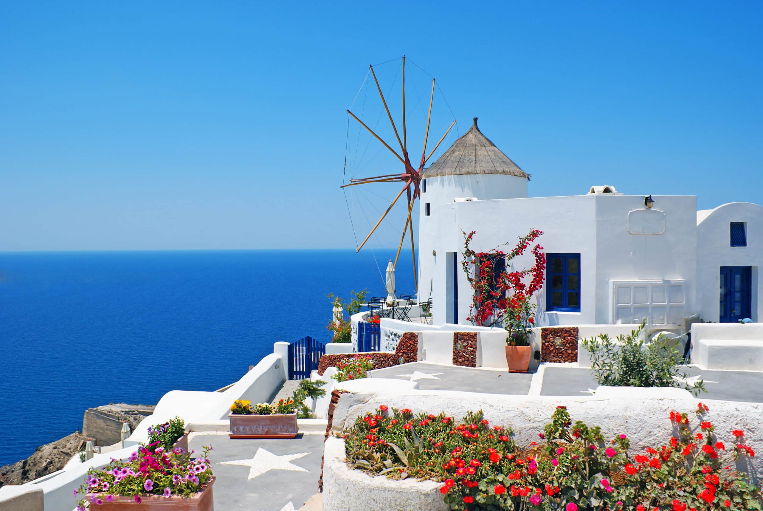 http://Moulin%20à%20vent%20blanc%20avec%20toit%20de%20chaume%20surplombant%20la%20mer%20Égée%20à%20Santorin,%20entouré%20de%20fleurs.