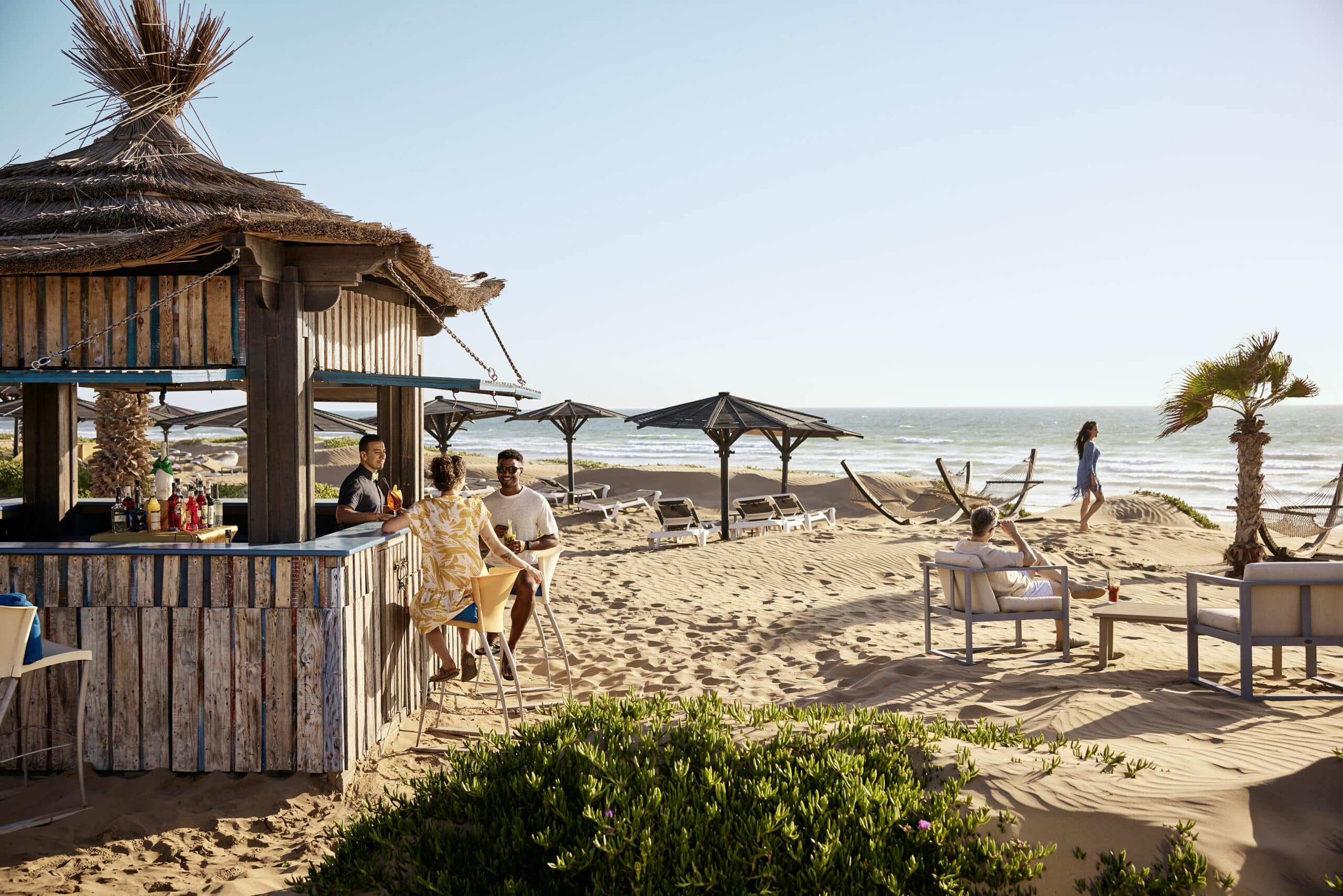 http://Bar%20en%20bois%20sur%20une%20plage%20avec%20des%20vacanciers%20profitant%20du%20soleil%20et%20des%20cocktails.