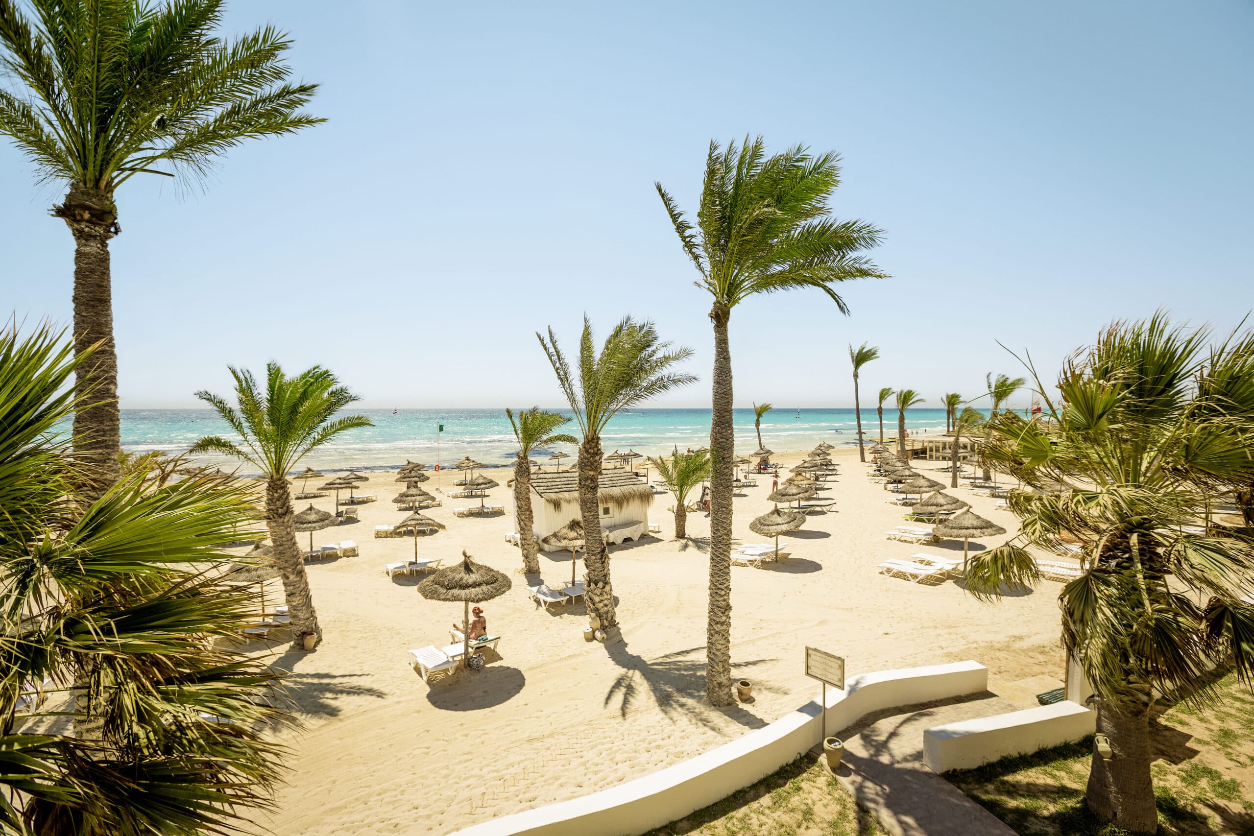 http://Plage%20de%20sable%20fin%20équipée%20de%20transats%20et%20parasols%20sous%20les%20palmiers.