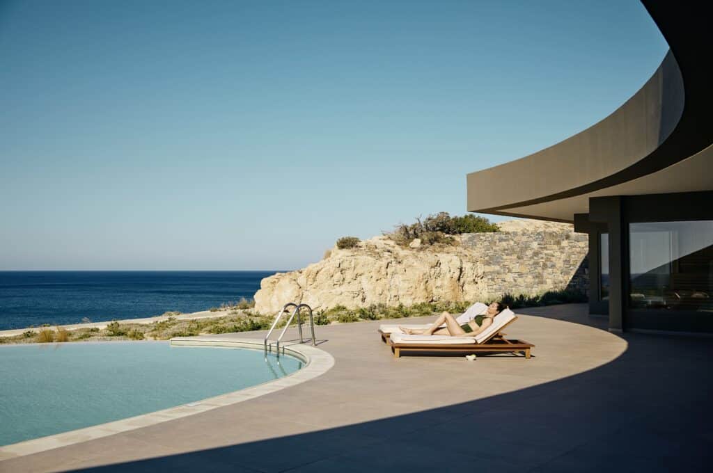 Femme allongée sur un transat au bord d’une piscine privée avec vue sur la mer.