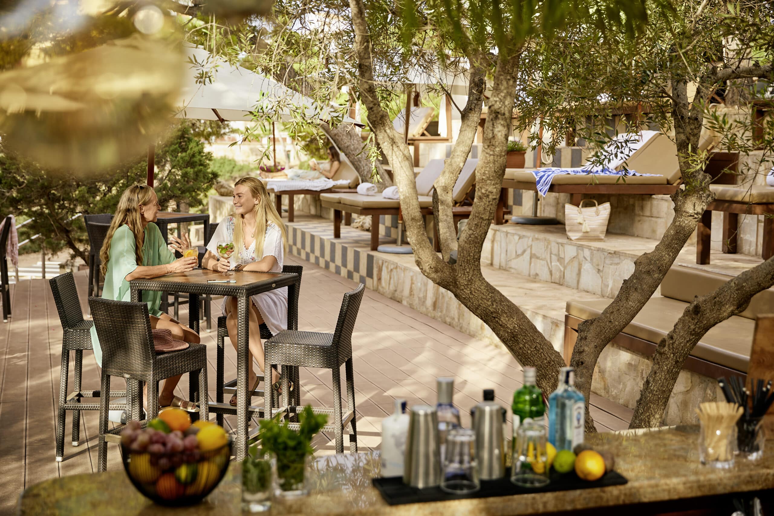 http://Deux%20femmes%20profitent%20de%20cocktails%20sur%20la%20terrasse%20ombragée%20d’un%20hôtel%20à%20Majorque.