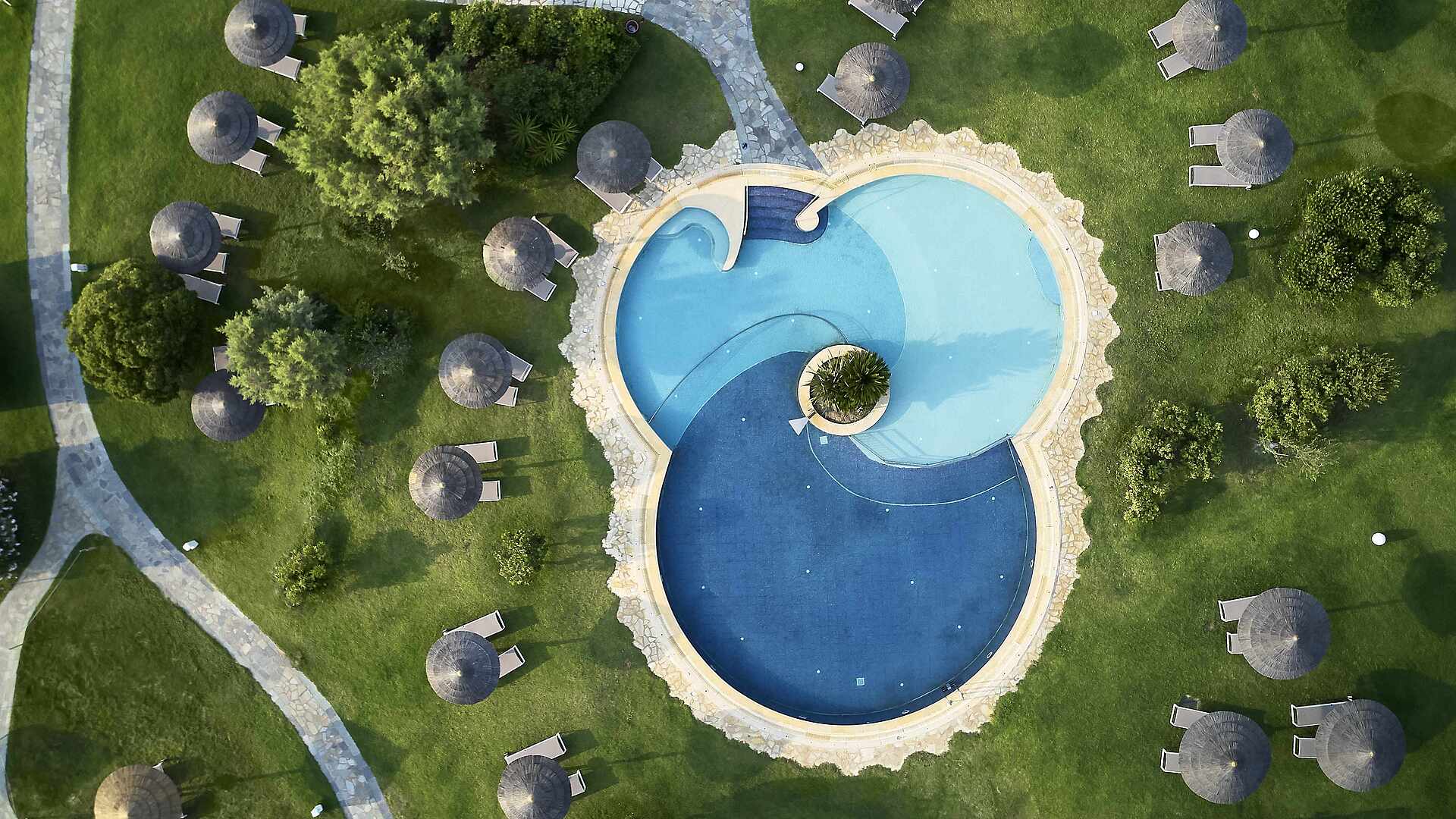 http://Piscine%20extérieure%20circulaire%20avec%20deux%20bassins%20vue%20du%20ciel,%20entourée%20de%20parasols%20sur%20pelouse%20verte.