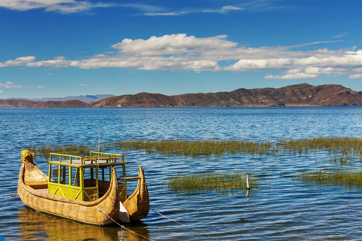 http://Bateau%20traditionnel%20en%20roseaux%20naviguant%20sur%20le%20lac%20Titicaca%20avec%20montagnes%20en%20arrière-plan