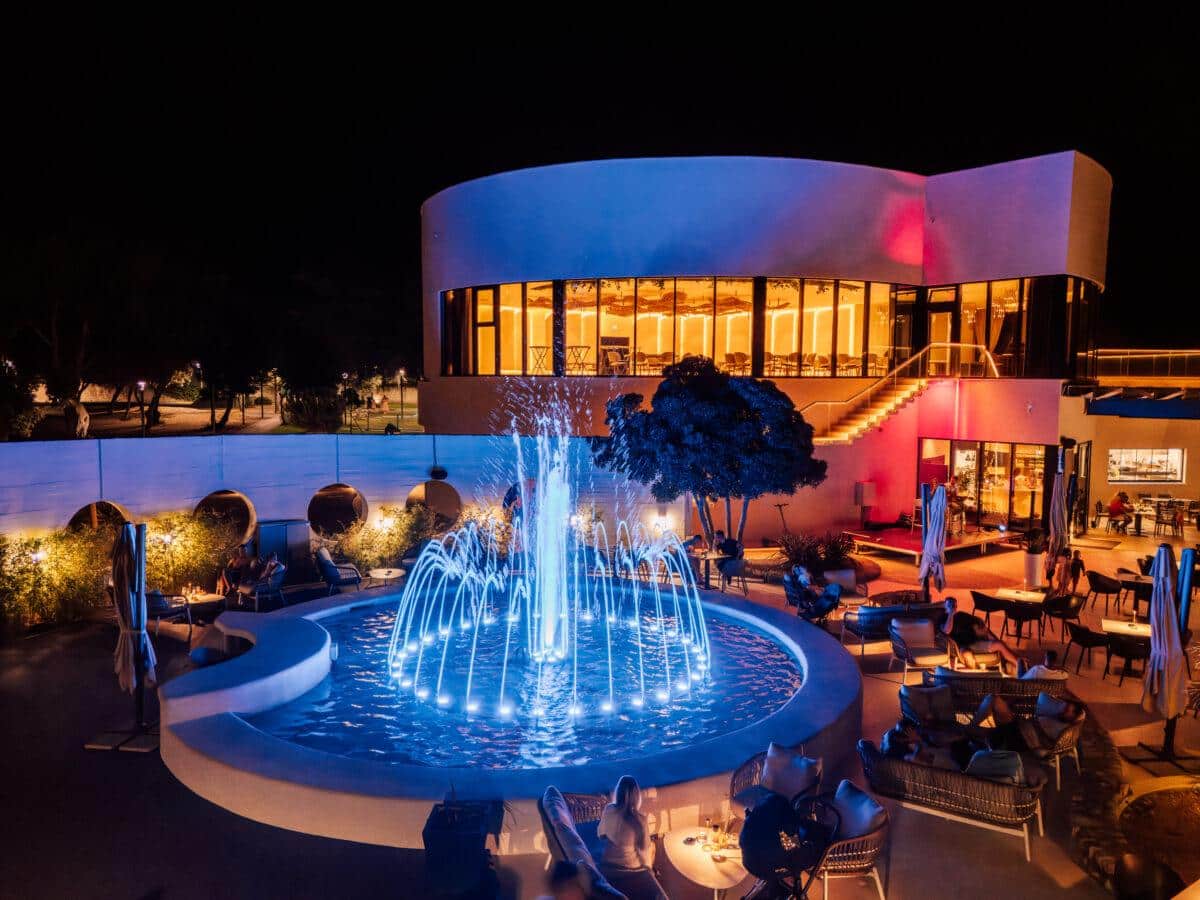 http://Terrasse%20d’hôtel%20avec%20fontaine%20lumineuse%20et%20espace%20lounge%20en%20soirée%20en%20Grèce