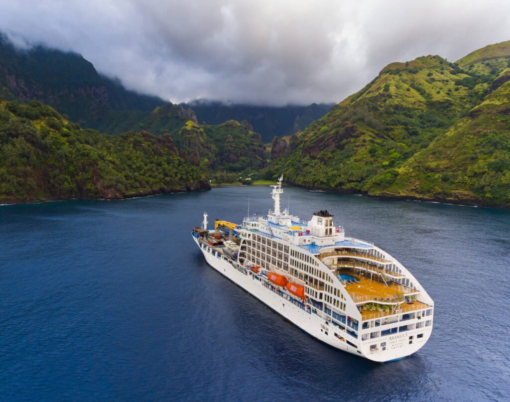 Bateau de croisière naviguant dans une baie entourée de montagnes verdoyantes sous un ciel nuageux