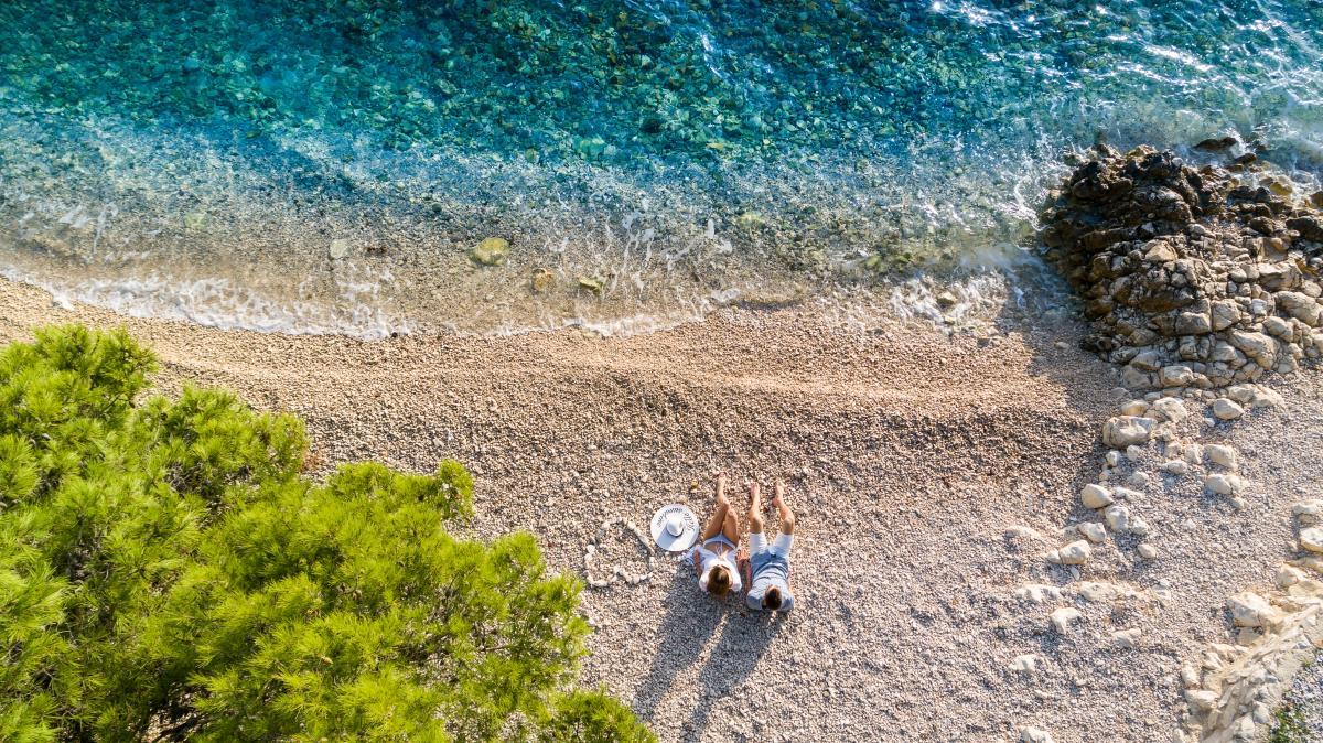 http://Vue%20aérienne%20d’une%20plage%20en%20Grèce%20avec%20eau%20turquoise%20et%20couple%20en%20bord%20de%20mer