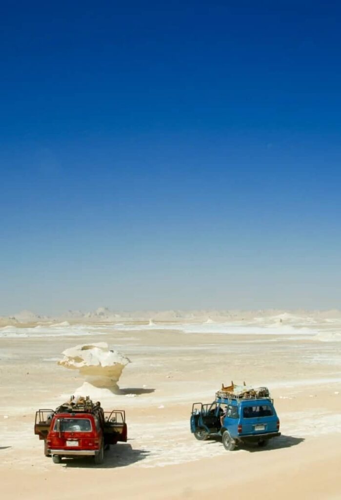 Deux véhicules 4x4 dans le désert blanc avec formations rocheuses et ciel bleu