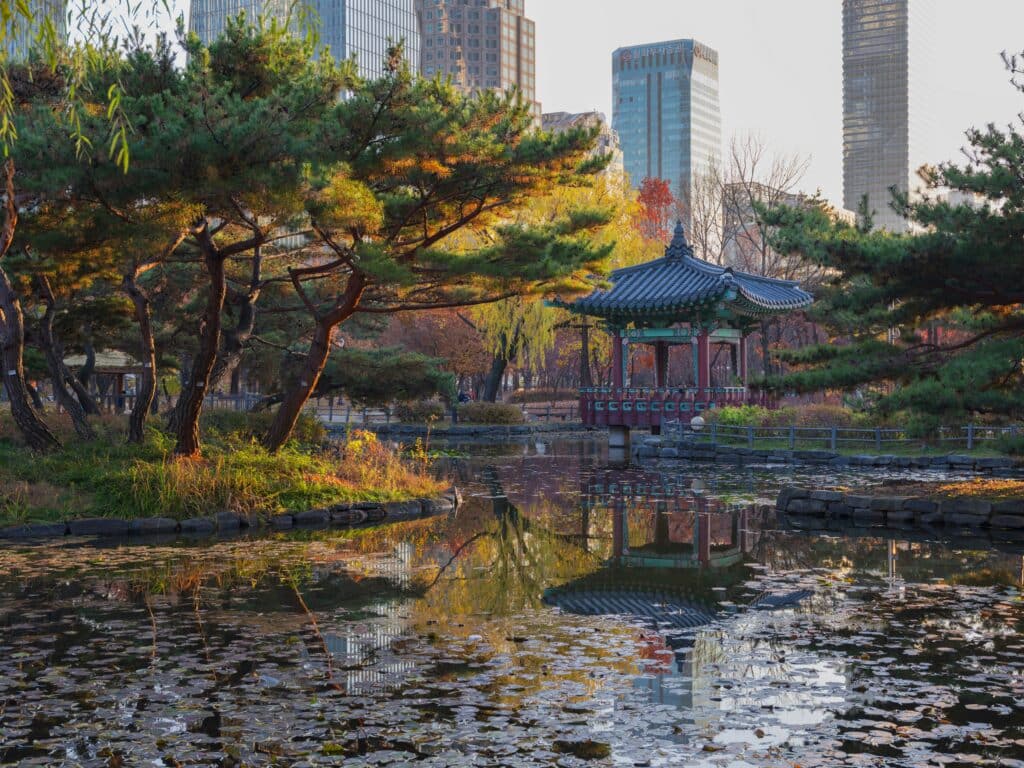 Pavillon traditionnel coréen au bord d'un étang dans le parc Songdo Central Park, avec les gratte-ciel d'Incheon en arrière-plan.