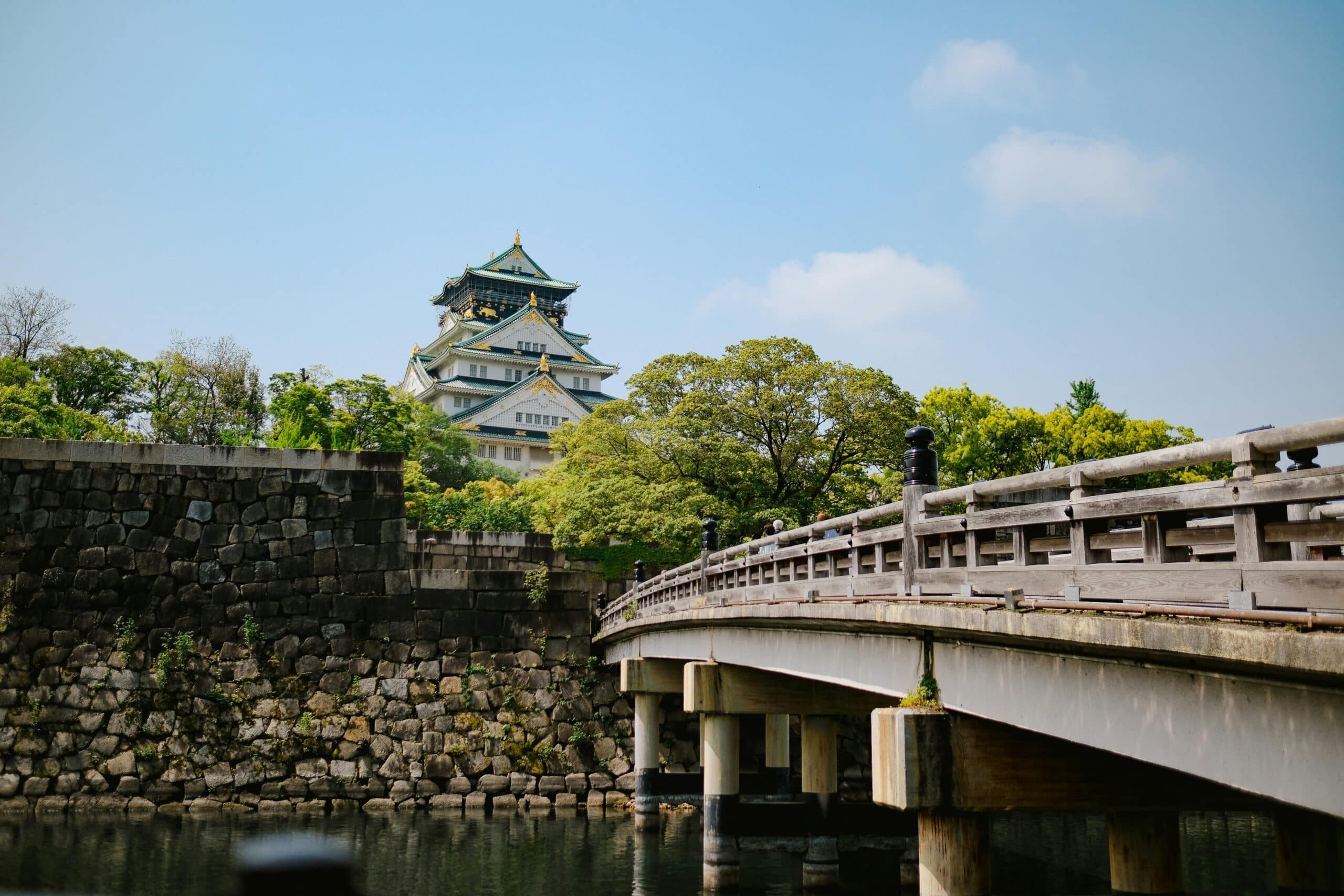 http://Château%20d’Osaka%20entouré%20de%20verdure%20avec%20un%20pont%20en%20bois%20au-dessus%20de%20l’eau