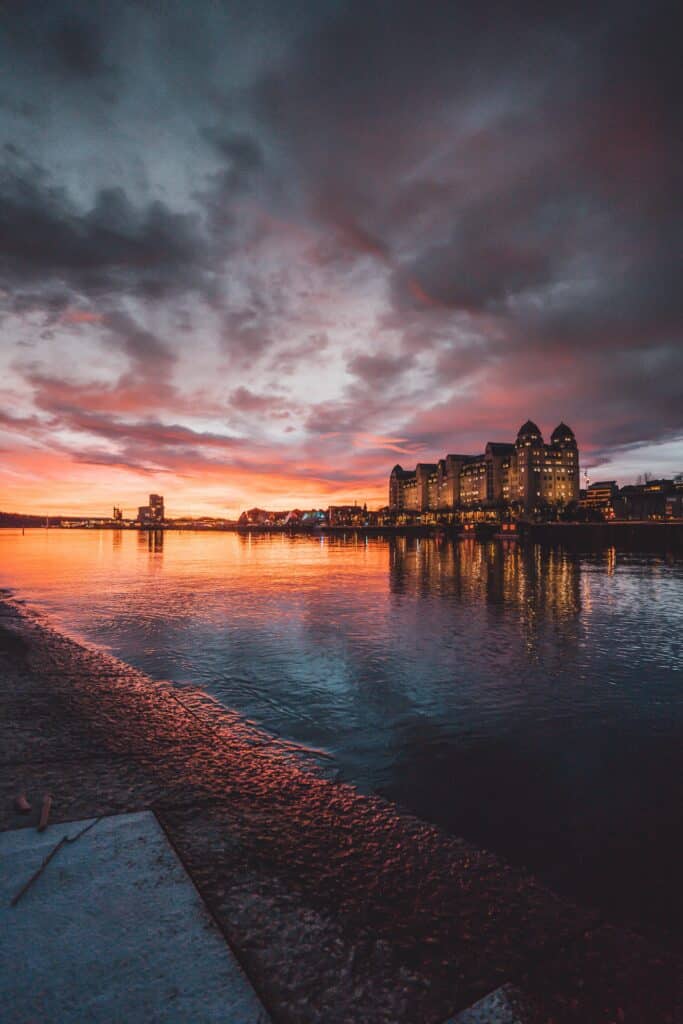 Coucher de soleil spectaculaire sur le port d’Oslo avec bâtiments illuminés et reflets sur l’eau